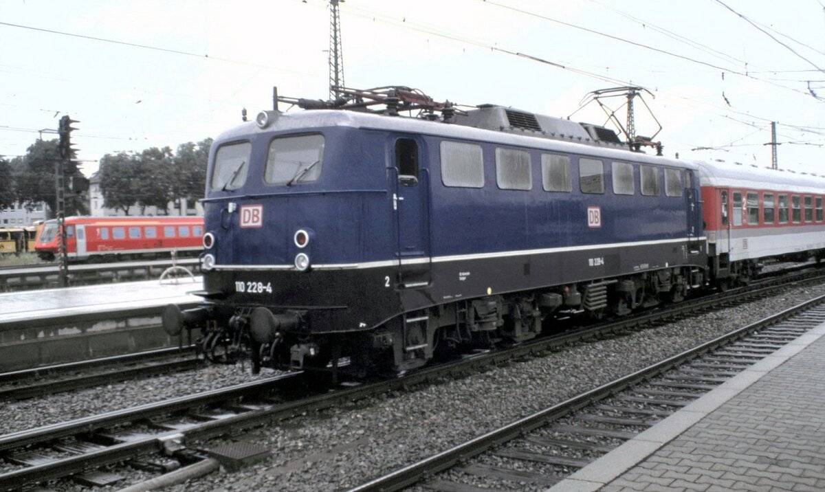 110 228-4 mit einem IC-Wagen; dahinter kommt ein IR-Wagen auf dem Durchgangsgleis in Ulm am 06.07.1999. Es ist mir leider nicht bekannt, ob es sich um einen Schadzug nach München-Feimann oder um Wagen zu einer Ausstellung handelt; letzteres würde ich vermuten.