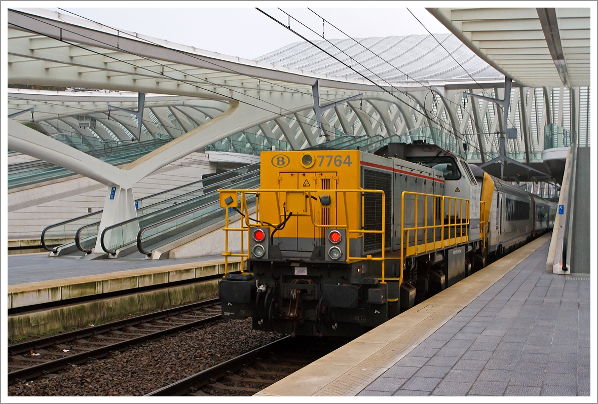 Auf der Bestandsstrecke liegt in der Ausfahrt des Bahnhofs L�ttich (Li�ge Guillemins), Richtung Br�ssel, eine Steigung von 35 Promille, darum muss bei langen IC-Z�gen eine Diesellok Schubhilfe leisten. Hier leistet die SNCB/NMBS HLD 7764  Toledo  am 23.11.2013 Schubhilfe. 

Die Lok wurde 2002 unter der Fabriknummer 1000981 bei Vossloh in Kiel gebaut, sie tr�gt die NVR-Nummer: 92 88 0077 064-8 B-B. 

Die HLD77 ist eine speziell auf die Belange der Belgischen Staatsbahn (SNCB) zugeschnittene Weiterentwicklung der G 1205. Zwischen 1999 und 2005 wurden insgesamt 170 Lokomotiven an die SNCB geliefert, zudem haben sie einen belgischen Anglo-Belgian Cooperation 6-Zylinder-Dieselmotor vom Typ 6DZC-1000-144A mit 1.150 KW Leistung.