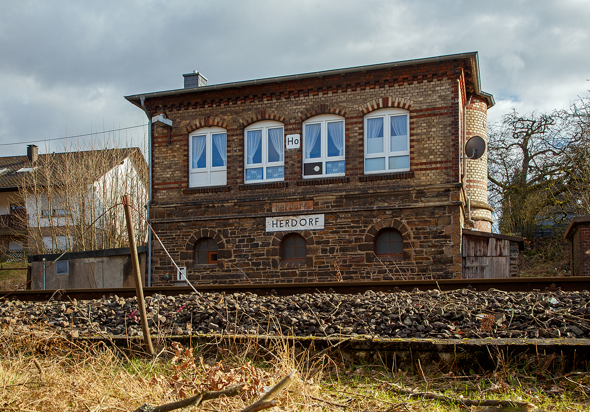 Das 1901 gebaute mechanische Weichenwärter Stellwerk Herdorf Ost (Ho), an der Bahnstrecke Betzdorf - Haiger (KBS 462, auch als Hellertalbahn bezeichnet), hier am 15.02.2022.

Ja, in Herdorf gibt es immer noch den Luxus von zwei in Betrieb befindlichen Stellwerken das Stellwerk Herdorf Fahrdienstleiter (Hf) und das hier zusende Weichenwärter Stellwerk Herdorf Ost (Ho). Sie liegen in Sichtweite ca. 500 m entfernt, Hf beim Bahnhof und hier Ho in der Nähe zum Abzweig zur Anschlussstelle KSW (ex Freien Grunder Eisenbahn). Bis in die 1960-Jahre waren die Aufgaben des Weichenwärters noch sehr umfangreicher. Die Strecke war noch eine zweigleisige Hauptstrecke. Ursprüngliche Planungen sahen sogar vor, sie im Rahmen der Elektrifizierung der Siegstrecke ebenfalls zu elektrifizieren. Diese Erwägungen wurden aber leider nicht weiter verfolgt. Zudem gab es noch Anschlussstellen zur Herdorfer Friedrichs Hütte und zu den Eiserfelder Steinwerken AG.  

Da die Stellwerkstechnik in Herdorf noch rein mechanisch ist, werden beide noch benötigt, bzw. ein Umbau auf ein Stellwerk ist wohl zu aufwendig. 

Im Dezember 2021 wurde bekannt, dass sich einiges an der Hellertalbahn verändern soll. Es sollen vier Halte wegfallen, die übrigen Haltepunkte in Rheinland-Pfälzischem Gebiet erneuert und neue Akkumulatortriebwagen (Akkutriebwagen - AT) eingesetzt werden, die dann auf der Strecke mit bis zu 100 km/h fahren können.  Da bin ich gespannt wann die Veränderung kommt.