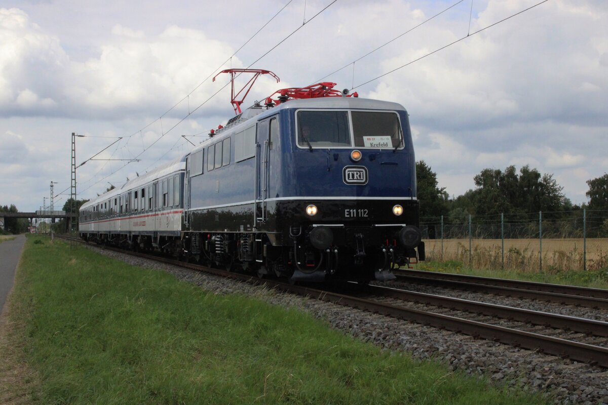Der Morgen von 23 Juli 2025 war noch etwas grau wann bei Kaarst vom offenbarer Weg TRI E11 112 samt RB37 nach Neuss Hbf fotografiert wurde.