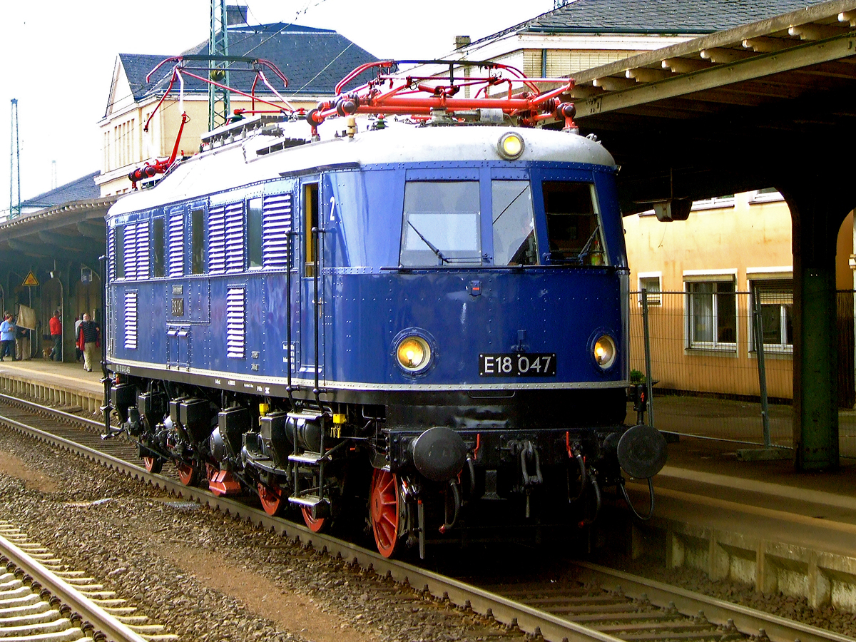E18 047 (DB 118 047-0, eingestellt als 91 80 6118 047-0 D-MEG) fährt am 01. Mai 2010 durch den Bahnhof Bebra.

Die Schnellzug-Elektrolokomotive wurde 1939 bei AEG unter der Fabriknummer 5161 gebaut.
Die Elektrolokomotiven der Baureihe E 18 (ab 1968 DB-Baureihe 118), gehörten zu den schnellsten Elektrolokomotiven der Deutschen Reichsbahn-Gesellschaft (DRG). Sie erreichte eine Höchstgeschwindigkeit von 150 km/h. Achsanordnung ist 1 Do' 1
Die Maschine ist im Besitz des Verkehrsmuseums Nürnberg.

Lebenslauft und Bezeichnungen:
1939-1949: DRB E 18 047 (Deutsche Reichsbahn)
1949-1968: DB E 18 047
1968-1984: DB 118 047-0
1984-1997: als Museumslok DB E 18 047 (BSW-Gruppe Würzburg)
1997-2005:  E 18 047 (DB Museum)
seit 2005: E 18 047 (DB Museum Nürnberg, Außenstelle Halle/Saale, eingestellt durch die MEG - Mitteldeutsche Eisenbahn GmbH (DB Cargo Tochter)

Die Lokomotiven der Baureihe E 18 waren bestimmt zur Beförderung schwerer Schnellzüge mit hohen Geschwindigkeiten. Die Lokomotiven wurden für die neu elektrifizierten Strecken München-Stuttgart und München-Nürnberg-Leipzig-Berlin entwickelt.

Im normalen Schnellzugdienst konnten die Maschinen 935-t-Schnellzüge in der Ebene mit 140 km/h, 990-t-Züge bei 5 Promille mit 100 km/h, 600-t-Züge bei 10 Promille mit 100 km/h und 360-t-Züge bei 20 Promille mit 75 km/h befördern.

Viele Baugruppen, wie zum Beispiel die Motoren oder der AEG Federtopfantrieb, wurden von der E 04 übernommen. Der Lokkasten hingegen war eine Neuentwicklung, der den Grundsätzen der Aerodynamik und der Stromlinie Rechnung trug. Die E 18 hatte keinen genieteten, sondern einen geschweißten Fahrzeugrahmen. Die Laufachsen waren für die Laufruhe mit der jeweils ersten – verschiebbaren – Treibachse in einem AEG-Kleinow-Gestell zusammengefasst. Der Antrieb erfolgte über Federtöpfe. Jeder Radsatz wurde über den verstärkt ausgeführte Kleinow-Federtopfantriebe von hochgelagerten Gestellmotoren Typ EKB860 angetrieben. Die ursprünglichen der Stirnfront angepassten Leuchten wurden bei der DB bis auf wenige Ausnahmen durch Einheitsleuchten ersetzt. 

Bedingt durch den Zweiten Weltkrieg wurde die weitere Beschaffung der E 18 zugunsten der wichtigeren Kriegsloks E 44 und E 94 eingestellt. Bis Kriegsende wurden daher nur 53 Lokomotiven gebaut. Nach dem Krieg verblieben bei der Deutschen Bundesbahn 41 Lokomotiven, die weiterhin im Schnellzugdienst eingesetzt wurden. Obwohl die Lokomotiven sich erwartungsgemäß gut bewährten und gute Laufeigenschaften auf geraden Strecken hatten, konnten sie im Bogenlauf nicht überzeugen und dieser war durch Reibung sogar teilweise ruckartig. Die optimale Einstellung der Hohlwellen und gute Wartung verbesserten die Laufgüte der Loks. Auch der spätere Einbau von Gummi-Parabelfedern statt der Federtöpfe brachte eine Verbesserung.

Mitte der sechziger Jahre wurden die leistungsfähigen Lokomotiven durch die neu in Auslieferung befindlichen E 10 verdrängt. Die Loks wurden nun vermehrt im Nahverkehr eingesetzt, was der Schnellzuglok nicht sonderlich bekam. Die Schäden an Schaltwerk und Bremse häuften sich. In den siebziger Jahren erhielten einige E 18 die Vorrüstung für die automatische Kupplung. Es wurden sogenannte Verschleißpufferbohlen angebracht, die das elegante Aussehen der Loks nachteilig beeinflussten. 

TECHNISCHE DATEHN:
Spurweite:  1435 mm (Normalspur) 
Achsformel:  1'Do1'
Länge über Puffer:  16.920 mm
Achsabstände: 2.800 / 2.100 / 3.000/  2.100 / 2.800 mm
Treibraddurchmesser: 	1.600 mm
Laufraddurchmesser: 	1.000 mm
Dienstgewicht:  108,5 t
Radsatzfahrmasse:  18,1 t
Höchstgeschwindigkeit:  150 km/h
Stundenleistung:  3.040 kW
Dauerleistung:  2.840 kW
Anfahrzugkraft:  206 kN
Treibraddurchmesser:  1.600 mm
Stromsystem:  15 kV 16 2/3 Hz AC
Anzahl der Fahrmotoren:  4 (Gestellmotore Typ EKB86
Antrieb:  Kleinow-Federtopfantrieb
Kupplungsart: Schraubenkupplung
