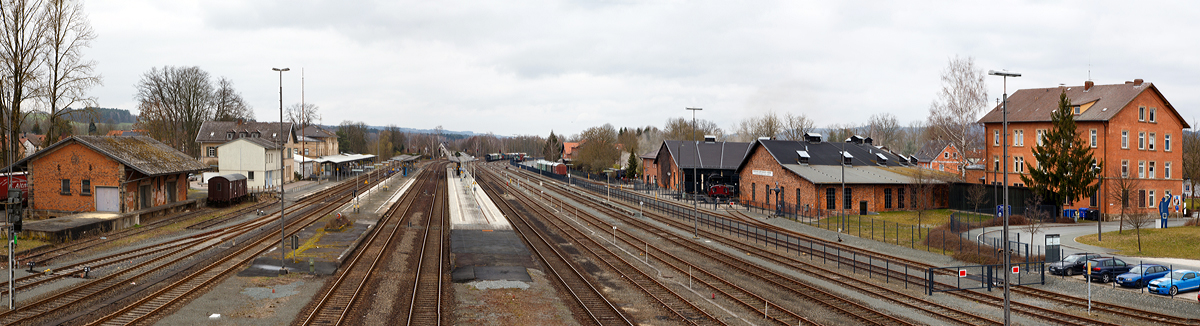 Ein �berblick �ber den Bahnhof Neuenmarkt-Wirsberg am 26.03.2016 (n�rdliche Blickrichtung).  

Links der alte G�terschuppen und das Empfangsgeb�ude, rechts das ehemalige Bahnbetriebswerk Neuenmarkt-Wirsberg, welches seit 1977 das Deutschen Dampflokomotiv Museum (DDM) beherbergt. 

Der Bahnhof liegt an den Bahnstrecken Bamberg–Hof (KBS 820 / KBS 850) und Bayreuth–Neuenmarkt-Wirsberg (KBS 852). Hinter dem Bahnhof in s�dlicher Richtung gabelt sich die Strecke, hier beginnt dann u.a. die bekannte Steilstrecke  Schiefe Ebene . Die Rampe nach Marktschorgast �berwindet auf 6,8 Kilometern L�nge 157,7 H�henmeter und hat eine durchschnittliche Steigung von 23 ‰ (max. 40 ‰). Diese war zu Dampflokzeiten eine Herausforderung f�r Mensch und Maschine, die meisten Z�ge mussten mit Schiebelokomotiven nachgeschoben werden. Daher erhielt der Bahnhof Neuenmarkt ein gro�z�gig dimensioniertes Bahnbetriebswerk.

Ich habe mal die Geoposition angegeben, in der Karte kann man dann die Streckenverl�ufe sehen.