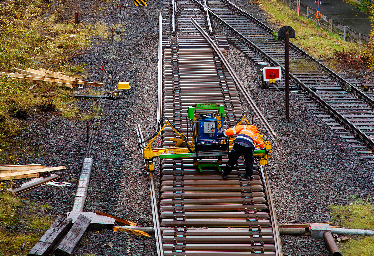 
Mittels einer hydraulischen Schienenumsetzmaschine vom Typ Giesmar MPRM 1032 werden am 15.10.2020 in Herdorf die letzten Meter Schienen auf die Schwellen gesetzt.

Die Schienenumsetzmaschine ist eine selbstangetriebene hydraulisch angetriebene Einheit zum Verlegen und Entfernen von langgeschweißten Schienen mit einem Bediener. Das Gerät stützt sich auf den Schwellen ab, die Schienen werden aufgenommen und können dann bis zu 500 mm angehoben werden. Nun erfolgt die seitliche Verschiebung und die Schienen werden auf die richtige Position auf der Schwelle abgelegt. Das Gerät ist geeignet für Scheinen mit einem Metergewicht von 37 bis 70 kg, die max. Hubkraft beträgt 4.500 kg. Es ist zudem möglich einen hydraulischen Schienenzieher ATR 6 anzuschließen. Das Eigengewicht von dem Gerät beträgt ca. 1.065 kg. 

Der hydraulische Antrieb erfolgt mittels einer HATZ-Hydraulikpumpen-Einheit (Hatz-Außenzahnradpumpe und Dieselmotor). Die Pumpe wird angetrieben von einem HATZ luftgekühltem Einzylinder-4-Takt Dieselmotor mit Direkteinspritzung und horizontale Kurbelwelle vom Typ 1D42C. 
