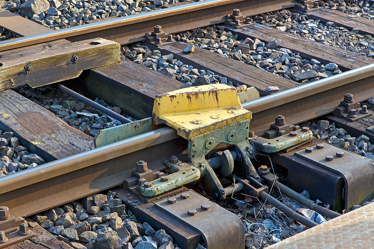 Nochmal Im Detail, die geschlossene Gleissperre hier an der Anschlu�stelle zum KSW-Gleis (Betriebsst�tte Freien Grunder Eisenbahn) in Herdorf am 20.03.2015. 

Das �berfahren einer aufgelegten Gleissperre f�hrt zum gewollten Entgleisen des Schienenfahrzeuges in die dem zu sch�tzenden Gleis entgegengesetzte Richtung. Der metallene Sperrklotz (Entgleisungsschuh) der Gleissperre kann nur durch Abheben eines Rades des Schienenfahrzeuges �berrollt werden und das Fahrzeug in der „Auswurfrichtung” seitlich von der Schiene weg und so zum Entgleisen bringen.