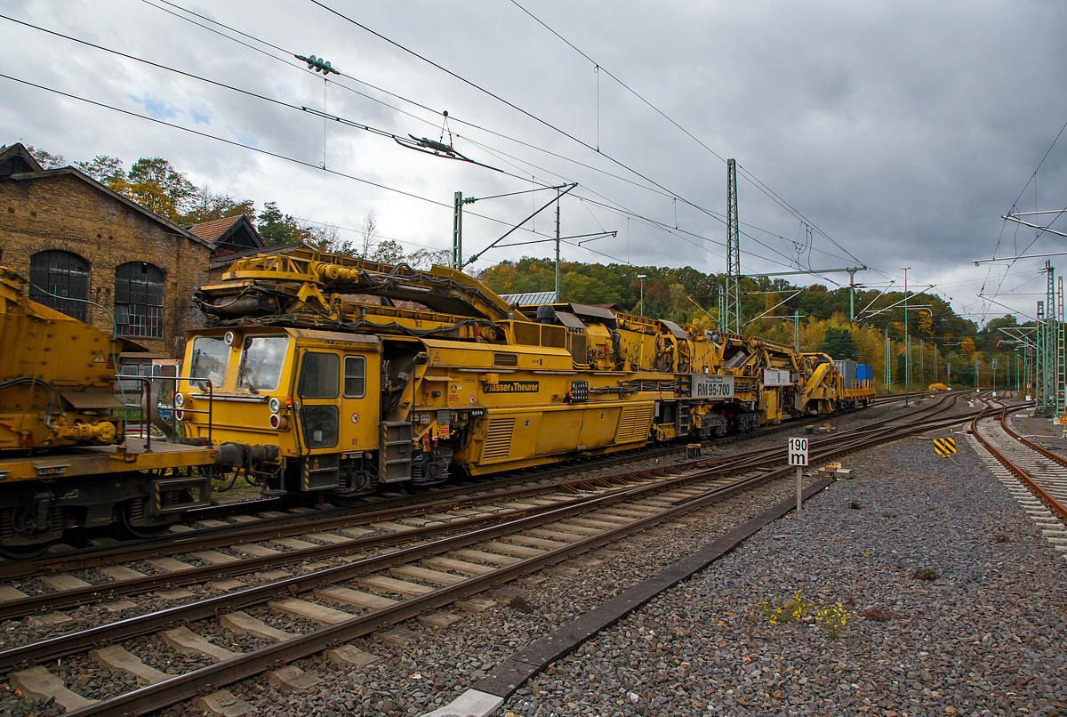 Plasser & Theurer Bettungsreinigungsmaschine RM 95-700
Die Plasser & Theurer Hochleistungs-Bettungsreinigungsmaschine RM 95-700, Schweres Nebenfahrzeug Nr. 99 80 9214 004-0 D-MGWB, ex 97 11 41 501 17-3, der MGW Gleis- und Weichenbau-Gesellschaft mbH & Co. KG (Berlin) am 22.10.2021 im Zugverband in Betzdorf (Sieg) bei einer Zugdurchfahrt.
 
Die Maschine wurde 2003 von Plasser & Theurer unter der Fabriknummer 4068 gebaut.

TECHNISCHE DATEN:
Bauart: RM 95-700
Spurweite: 1.435 mm (Normalspur)
Achsfolge:Bo´+Bo´Bo´+2´
Achsanzahl:  8
Länge: 48.240 mm
Drehzapfenabstände: 18.300 / 22.040 mm
Achsabstand im Drehgestell: 1.800 m	
Raddurchmesser: 920 mm (neu)
Höhe:  4.300 mm
Breite: 3.150 mm
Eigengewicht: 170,0 t
Motorengesamtleistung: 700 kW
V-Max Eigenfahrt:   20 Km/h
V-Max Zugverband: 100 Km/h
Zugkraft am Zughaken im Arbeitsbetrieb: ca. 300 kN
Streckenklasse: 	D4
zur Mitfahrt zugel. Personen: 4
Anhängelasten (Eigenfahrt):  40 t 
Anhängelasten (Arbeitsfahrt bei 10 ‰ Steigung):  1.000 t
Bremsarten: KE G – P mZK und D2b 
Handbremsgewicht: 30 t 
Kleinster befahrbarer Radius: 120 m

Besondere Ausstattung:
•Laser-Anlage zur genauen Steuerung der Reinigungstiefe bei Ablage des Gleises in Hochlage
•Reinigungsbreite von 3.800 mm bis 5.000 mm durch Ergänzungsbalken
•maximale Veschiebung Gleisrost +/- 30 cm
•Leistung bis zu 700 m³/h
•Dokumentation der Lage des Gleises hinter der Reinigungsmaschine durch MKS-Messschrieb  
•Automatisches Warnsystem für Maschinenwarnung (AWS)
•Neuschotterzuführung zur optimalen Verfüllung des gereinigten Gleises mit Schotter

RM 95-700 - Bettungsreinigung mit Doppelsiebanlage
Die RM 95-700 ist eine achtachsige, vollhydraulische Hochleistungsbettungsreinigungsmaschine mit Neuschotterzuführung in Gelenkbauweise, für den Einsatz auf dem Gleisnetz der DB AG. Der Antriebs- und Siebwagen fährt vorne auf einem zweiachsigen und hinten auf vierachsigem Triebdrehgestell (2x2 Doppeldrehgestell). Der Aushub- und Einschotterteil ist vorne am Antriebswagen angelenkt und fährt hinten auf einem Laufdrehgestell.

Materialaushub
Die Aushubkette ist eine Weiterentwicklung der weltweit bewährten Ketten von Plasser&Theurer und wurde hinsichtlich der Lebensdauer weiter optimiert. Sie ist als endlose Fünfecks-Kratzerkette mit einer Höhe von 300 mm ausgeführt. Die Kettengeschwindigkeit ist stufenlos im Bereich von ca. 1,8 bis 3,5 m/sec verstellbar, die maximale Räumtiefe beträgt 1.000 mm unter SOK der überhöhten Schiene. Die Maschine ist mit einem Räumbalken für eine Reinigungsbreite von 4 Meter ausgestattet. Für geringere Räumbreiten wird ein Kettenquerbalken mit 3,4 m geliefert. Der hydraulische Kettenquerbalkenverschluss vereinfacht den Einbau des Querbalkens und verringert wesentlich die erforderlichen Rüstzeiten. Im Bereich der Räumkette ist die kontinuierlich arbeitende Gleishebe- und Rückeinrichtung angeordnet. Die maximale Hebung beträgt 250 mm, die maximale seitliche Gleisverschiebung ± 300 mm.

Siebanlage
Die Maschine ist mit zwei robusten Schwingsieben mit einer Gesamtfläche von über 40 m2 ausgestattet, die für höchste Qualität und Leistung sorgen. In der Überhöhung in Bögen verstellt der Maschinist die Querneigung der Siebanlage hydraulisch um bis zu 160 mm, sodass die Siebe immer waagrecht bleiben. Der Abraum gelangt über Förderbänder zur Maschinenfront. Das Übergabeförderband ist drehbar ausgeführt, sodass kein Schutzwaggon für Überstellfahrten notwendig ist. Der Abraum kann seitlich neben dem Gleis, auf am Parallelgleis stehende Waggons oder auf ein von der Maschine geschobenes Abraumverladesystem abgeladen werden.

Schotterverteileinrichtung
Der gereinigte Schotter gelangt von der Siebeinrichtung über Förderbänder in einen Schotterspeicher und von hier aus über ein Bodenförderband, einen Schotterschacht und ein Einschotterungsband direkt hinter der Räumkette in den Gleisbereich. Der Schotterspeicher und die Förderbänder auf der Aushubmaschine ermöglichen einen Mengenausgleich bei Arbeitsbeginn und Arbeitsende. Der Einschotterpflug mit verstellbaren Pflugschildern sorgt für eine gleichmäßige Verteilung des gereinigten Schotters.

Neuschotteranlage
Mit der RM 95-700 ist die Zuführung von Neuschotter im Zuge der Bettungsreinigung möglich. Dazu wird der Neuschotter von den hinten angereihten Materialförder- und Siloeinheiten in den Zuführungsschacht gefördert, und über die verstellbaren Einschotterhosen die Stopfzonen gezielt eingeschottert.

Lasereinrichtung, elektronischer Schreiber
Die präzise Führung der Räumkette in Längs- und Querrichtung ist von entscheidender Bedeutung für die Arbeitsqualität bei der Bettungsreinigung. Daher wird mit einer Lasereinrichtung die Bezugsbasis für die Steuerung von Räumtiefe und Kettenquerneigung vergrößert, um einen noch präziseren Schnitt zu gewährleisten. Diese Lasereinrichtung besteht aus einem Lasersender, der in einer Entfernung von bis zu 300 m (abhängig von Gleisgeometrie und Sichtverhältnissen) aufgestellt wird, und einem Laserempfänger an der Maschine. Der Empfänger wird entsprechend der Wahl des Bezugsstranges links oder rechts auf Konsolen an der Kettenführung positioniert. Die Voreinstellung der Räumtiefe erfolgt durch den Maschinisten von der Arbeitskabine aus. Hier steht auch eine Anzeige für Räumtiefe und ein Zeigerinstrument für die Planumsneigung zur Verfügung. Weiter ist die Maschine mit einem digitalen Vierkanal-Schreiber ausgestattet, womit folgende Parameter aufgezeichnet werden:
Räumtiefe
Planumsneigung
Überhöhung des gereinigten Gleises 
Verwindung des gereinigten Gleises

Kabinen
Alle Kabinen sind geschlossen, schallisoliert und vibrationsgedämpft ausgeführt. Gute Sichtverhältnisse sind gewährleistet. Kabinenheizung, Kabinenlüfter mit Luftfilter sowie Klimaanlagen (optional) sorgen für komfortable Bedingungen bei unterschiedlichen klimatischen Bedingungen während des Arbeitseinsatzes. In allen Kabinen ist außerdem eine Wechselsprechanlage installiert. Vorne und hinten befindet sich jeweils eine Fahrkabine mit den Bedienungselementen für Rangierfahrten. Direkt vor der Räumkette befindet sich die Arbeitskabine. Sie enthält sämtliche Bedienungselemente für die Kette, Hebe- und Rückeinrichtung, Arbeitsvorschub etc.

Die RM 95-700 ist eine Maschine für viele Einsatzmöglichkeiten
Mit der RM 95-700 steht eine Maschine zur Verfügung, die aufgrund ihres Konzeptes bei unterschiedlichen Baustellensituationen flexibel eingesetzt werden kann. Die RM 95-700 bietet dabei eine Reihe von Vorteilen:
•Hohe Arbeitsleistung durch die hohe Siebleistung
•Präziser Planumsschnitt durch Lasersteuerung
•Integrierte Neuschotterzuführung, damit ausreichender Schotter auch für die Ein- und Ausbaustelle und somit eine besser Nutzung der Sperrpausen
•Kurze Materialtransportwege innerhalb der Maschine
•Schotterspeicher für Materialmengenausgleich bei Baustellenanfang und Baustellenende
•Kurze Rüstzeiten durch hydraulischen Kettenquerbalkenverschluss und Montagekran
•Hohe Zugkraft durch drei angetriebene Drehgestelle
•Robuste Konstruktion des Maschinenrahmen
•Leistungsfähige Räumkette


Quelle: MGW Gleis- und Weichenbau-Gesellschaft mbH & Co. KG 
