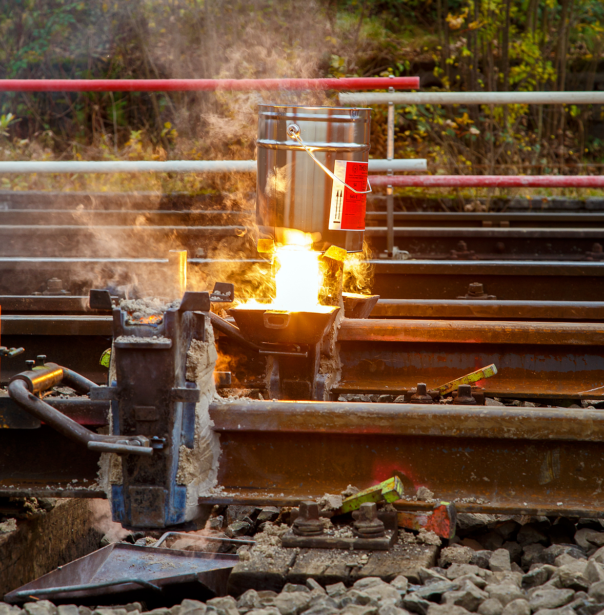 
Thermitschweißen am 31.10.2020 an der Hellertalbahn (KBS 462 / DB-Streckennummer 2651) hier Gleis 1 vom Bahnhof Herdorf.

Bild 5 – Nachdem die Form gefüllt ist, läuft der flüssige Rest (Stahl, Aluminiumoxid und Schlacke) in die seitlichen Schlackenschalen ab.