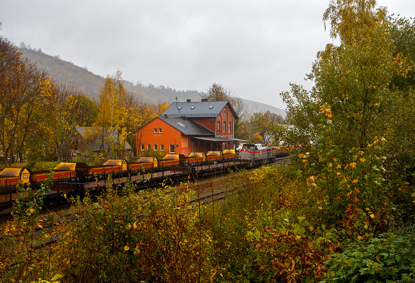 Baustelle Bahnhof Herdorf am 25 Oktober 2025, es sch�ttete ohne Unterlass, dazu noch heftige Windb�en, aber die Arbeiten zur Erneuerung der Weiche 3 und der R�ckbau mit L�ckenschluss f�r die drei aufeinander folgenden Weichen 22, 23 und 24 (Erneuerung Anschluss von Weiche 26 an Gleis 4) haben begonnen. So musste ich doch dem widrigen Wetter an die Strecke. 

Bei dem Wetter haben die Gleisbauarbeiter mein vollstes Mitgef�hl. Da haben es die Lokf�hrer und Baggerfahrer durch den Schutz ihrer Kabine schon besser. 

Hier seht u.a. die 271 022-6 „Charlotte“ (92 80 1271 022-6 D-KAF) eine Vossloh/MaK G 1000 BB der KAF Falkenhahn Bau AG. ex MRCE bzw. ex HGK DH 49, mit einigen Flachwagen. Hinten auf Gleis 1 steht sehr langer Schotterzug (ca. 600 m) an dessen Ende die Vossloh G 12 – 4120 001-7 „Karl August“ (92 80 4120 001-7 D-KAF) befindet. 