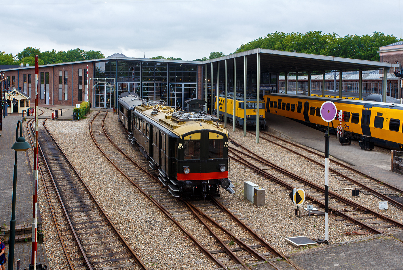 Der NS Mat ’24-Triebwagenzug (BD 9107, C 8553 und C 8104) „Blokkendozen“ (Kastendose) am 24 Juni 2025 im Het Spoorwegmuseum (bis 2005 NSM - Nederlands Spoorwegmuseum / Niederl�ndischen Eisenbahnmuseum) in Utrecht im ehemaligen Bahnhof Maliebaanstation. Ein Eisenbahnmuseum das zum Verweilen einl�dt. Der dreiteilige Zug vom Typ Mat’24 des Niederl�ndischen Eisenbahnmuseums besteht aus BD 9107, C 8553 und C 8104

Der Triebwagen BD 9107 (mBD):
Hier im Vordergrund der Triebwagen NS BD 9107 (mBD). Er wurde 1927 von Beijnes, offiziell Koninklijke Fabriek van Rijtuigen en Spoorwagens J.J. Beijnes (K�nigliche Fabrik f�r Kutschen und Eisenbahnwagen J.J. Beijnes) in Haarlem, mit einer elektrischen Ausr�stung von Metropolitan Vickers, gebaut und an die NS - Nederlandse Spoorwegen geliefert. Er hat 40 Sitzpl�tzen der zweiten Klasse sowie ein Gep�ckabteil. Seine Historischen Nummer waren ab 1927: BD 9007 / 1931: BD 9107 / 1946: CD 9107 / 1958: BD 5902 / 1966: 159016 / 1968: 9741937 / 1989 BD 9107.

Der Wagen kehrte Ende 1945 in besch�digtem Zustand aus Deutschland zur�ck. Er wurde 1947 instandgesetzt und als CD 9107 (mCD) wieder in Betrieb genommen. In den Jahren 1957/58 erfolgte der Umbau zu einem antriebslosen Wagen (BD 5902/BDz), dabei wurde die Inneneinrichtung der zweiten Klasse im „neuen Stil“ eingebaut, wobei die Anzahl von 40 Sitzpl�tzen erhalten blieb. Die elektrische Ausr�stung (einschlie�lich der Stromabnehmer) wurde entfernt, der F�hrerstand durch eine Plattform mit �bergangsfaltenbalg ersetzt und das Gep�ckabteil um einen Seitengang erweitert. Nur vier Jahre sp�ter wurde der Wagen �berfl�ssig und zur Nummer 159016, einem Schulungswagen f�r die Abteilung Gleisbau und Infrastruktur, umgebaut. Nach der Fertigstellung eines festen Schulungsraums im Jahr 1987 wurde der Wagen f�r die museale Erhaltung vorgesehen.

Die Restaurierung und der Umbau wieder zum Elektrotriebwagen BD 9107 erfolgten zwischen 1987 und 1989 im Ausbesserungswerk Amersfoort, dabei wurde das Fahrzeug weitgehend nach den Originalspezifikationen der 1930er Jahre hergerichtet, jedoch mit einer elektrischen Anlage der Firma Heemaf ausgestattet. Im Mai und Juni 2010 wurde der BD 9107 mit einer vereinfachten Version des automatischen Zugbeeinflussungssystems (ATBe) ausger�stet und im Strukton-Werk in Zutphen �berpr�ft. Die Betriebszulassung erfolgte im September, gefolgt von einer ersten Fahrt f�r die Ehrenamtlichen des Eisenbahnmuseums am 9. Oktober 2010. 

Im November 2011 wurden der BD 9107 und der Barwagen C 8553 zur �berholung der Fahrwerke in das NedTrain-Werk nach Haarlem �berf�hrt. Die eigentliche Aufarbeitung der Drehgestelle �bernahm die Firma Reuschling in Hattingen (Deutschland), dabei wurden unter anderem s�mtliche Tragfedern durch neue ersetzt. Im Dezember 2012 erhielt der gesamte Zug nach einer erfolgreichen Probefahrt im �ffentlichen Streckennetz die erneute Betriebszulassung. Der „Blokkendoos“-Zug ist aber derzeit aufgrund umfangreicher Instandhaltungsarbeiten au�er Betrieb.

Die NS-Baureihe Mat ’24 oder Materieel ’24 war eine (die erste) Serie von Elektrotriebz�gen, die von der NS - Nederlandse Spoorwegen (Niederl�ndischen Staatsbahnen, heute Niederl�ndische Eisenbahnen AG) ab 1924 in gro�er Zahl eingesetzt wurde. Diese Z�ge sind unglaublich robust und schwer. nd der Tatsache, dass die Trainer wie Bausteine zusammengestellt werden k�nnen. Im Volksmund erhielten sie wegen des eckigen �u�eren und der Tatsache, dass die Wagen wie Bausteine zusammengestellt werden konnten, den Spitznamen „Blokkendozen“ (Kastendose). Ein weiterer Spitzname war „buffermaterieel“, weil sie im Unterschied zu anderen, mehr windschl�pfig aussehenden elektrischen Triebz�gen mit �blicher Schraubenkupplung versehen waren. Wegen der Verbindung �ber Schraubenkupplung mit zwei Puffern konnten die Einheiten sehr flexibel kombiniert werden. Meist bestand ein Zug aus zwei Triebwagen und zwei oder drei antriebslosen Mittelwagen. Die lauten Ger�usche der Motoren und Antriebe erinnerten manche Fahrg�ste an Staubsauger, so dass auch dieser weitere Spitzname  Staubsauger  verwendet wurde. 

Ab Mitte der 1950er Jahre wurden die Mat ’24 zunehmend durch die neue Baureihe Mat ’54 ersetzt. Der letzte elektrische „Blokkendoos“-Zug verkehrte am 31. Mai 1959. Einige Wagen blieben als Reisezugwagen bis 1973 im Einsatz, sie wurden unter anderem in Milit�rz�gen sowie zur Kapazit�tserweiterung w�hrend der Hauptverkehrszeiten verwendet. Bei einigen Triebwagen wurden die Stromabnehmer und Motoren demontiert, sie wurden auch als einfache Beiwagen weiterverwendet. Da die Mat ’24 sehr robust waren, wurden einige Einheiten sp�ter auch als Postwagen oder f�r Dienstzwecke eingesetzt. Mehrere Wagen blieben museal erhalten.

TECHNISCHE DATEN Triebwagen BD 9107 (mBD):
Baujahr: 1927
Spurweite: 1.435 mm (Normalspur)
L�nge �ber die Puffer:	19.800 mm
Achsfolge:	Bo'Bo'
Achsabstand im Drehgestell: 2.500 mm
Treibraddurchmesser: 1.000 mm (neu)
Eigengewicht: 59.000 kg
Tragf�higkeit Gep�ckraum: 2,5 t
Traktionsmotoren: 4 St�ck vom Typ Heemaf TM 8
Stundenleistung: 4 x 136 = 544 kW (Urspr�ngliche Leistung 661,5 kW)
Dauerleistung: 4 x 100 = 400 kW
�bersetzung: 27 : 56
H�chstgeschwindigkeit: 100 km/h
Kupplung: Schraubenkupplung (UIC-Kupplung)
