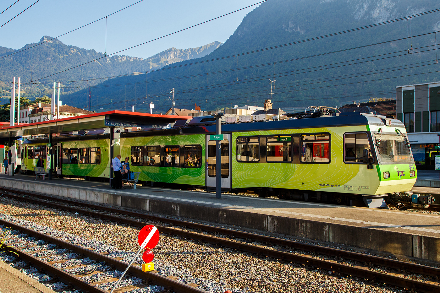 Der tpc AOMC / ASD) Beh 4/8 591, ein elektrischer Doppeltriebwagen für den gemischten Zahnrad- und Adhäsionsbetrieb steht im Bahnhof Aigle als ASD Regionalzug R 24 zur Abfahrt nach Les Diablerets bereit. Wobei den Zahnradantrieb („h“) brauch er auf der 23,3 Kilometer langen Strecke der ASD (Aigle–Sépey–Diablerets) nicht, denn sie ist eine reine Adhäsionsbahn und führt von Aigle über Le Sépey nach Les Diablerets.

Die beiden Doppeltriebwagen Beh 4/8 591–592 wurden 2001 von Bombardier, ex Vevey ACMV (Wagenkasten), Stadler (Drehgestelle/Zahnradtechnik) und Adtranz (Elektrik) gebaut und an die tpc für den Betriebsteil AOMC geliefert. Damals war dort noch unter 950 V Gleichspannung (DC) und mit dem Zahnstangensystem Strub gefahren. 

Im Sommer 2016 wurde die AOMC Strecke umfassend modernisiert. Dabei wurden die Zahnstangenabschnitte vollständig erneuert und das bisherige Zahnstangensystem Strub durch das Zahnstangensystem Abt ersetzt. Die Fahrleitungsspannung von 950 V wurde nun auf 1500 V Gleichspannung (DC) erhöht. Somit besitzen alle ab Aigle verkehrenden Strecken der TPC das gleiche Zahnstangensystem (wobei die ASD keine Zahnstange hat) und die gleiche Spannung. Der Verkehr wird nun meist vollständig mit den neu abgelieferten Beh 2/6 541–547 abgewickelt. Von den bestehenden Triebfahrzeugen der AOMC wurden einzig die beiden im Jahr 2001 gelieferten Doppeltriebwagen Beh 4/8 591–592 an das neue Zahnstangen- und Stromsystem angepasst.

So erfolgte im Jahr 2016 bei Stadler der Umbau der beiden Beh 4/8 591–592 auf 1.500 V DC mit neuem Umrichter, die Trieb- und Bremszahnräder wurden (von Strub zu Abt) ersetzt. Die Fahrmotoren konnten ohne eine Neuwicklung beibehalten werden.

Vermutlich können die Doppeltriebwagen aber nicht auf den Zahnstangenabschnitten der AL (Aigle–Leysin-Bahn) fahren, denn diese haben eine Neigung bis zu 230 ‰, die AOMC (wofür die Treibwagen gebaut wurden) hat ja eine maximale Neigung von 135 ‰. 

TECHNSCHE DATEN:
Baujahr: 2001 (Umbau 2016)
Spurweite: 1.000 mm (Meterspur)
Achsfolge: Bo'zz 2' + 2' Bo'zz
Zahnradsystem:  Abt (bis 2015 Strub)
Länge über Puffer : 35.200 mm
Eigengewicht: 58,5 t (bis 2015 55,1t)
Zul. Höchstgeschwindigkeit (Adhäsion): 80km/h 
Zul. Höchstgeschwindigkeit (Zahnradbetrieb): 30 km/h bei Bergfahrt 
Max. Neigung : 135 ‰
Sitzplätze: 96 
Stehplätze: 70 
Stromsystem: 1.500 V DC (Gleichstrom) (950 V DC bis 2015)
Stromabnehmer: 2
Bremse: Frein P + Mg-A
