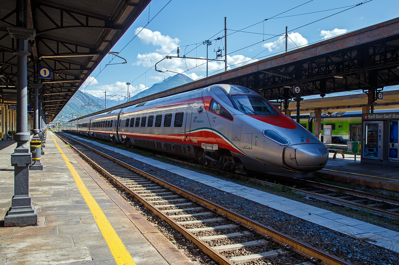 Der Trenitalia  Frecciargento“  ETR 610.004 (93 85 5 610 004-9 CH-TI) der Trenitalia (100-prozentige Tochtergesellschaft der Ferrovie dello Stato) hat am 26. Mai 2023, als EC 32 (Milano Centrale – Domodossola – Genève (Genf), den Bahnhof Domodossola erreicht.

Hier Bahnhof Domodossola findet dann ein Zug-Personalwechsel statt, die SBB übernimmt den Zug von der Trenitalia.
