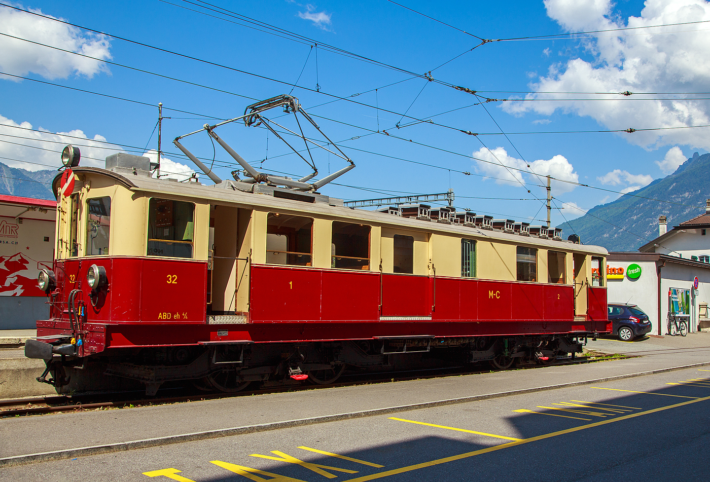 Der wunderschöne ehemalige Martigny-Châtelard-Bahn (MC) Triebwagen ABDeh 4/4 32  le tracteur  ( der Traktor ) vom Verein Train Nostalgique du Trient, ex MC BCFe 4/4, ex SBB CFeh 4/4 N°32 Baujahr 1921, am 26. Mai 2023 im Bahnhof Martigny.

Der Förderverein TNT Train Nostalgique du Trient wurde 1995 wurde 1995 gegründet, dieser bezweckt die alten Fahrzeuge der Schmalspurbahn Martigny-Châtelard-Bahn (MC) im betriebsfähigem Zustand zu halten.

Der meterspurige elektrische Personentriebwagen mit Gepäckabteil für gemischten Zahnrad- und Adhäsionsbetrieb ABDeh 4/4 32 wurde 1921 als CFeh 4/4 für die SBB (für Materialtransporte von der SBB-Station Martigny zum MC-Bahnhof Le Châtelard-Giétroz) gebaut. Während der Arbeiten am Barberine-Staudamm der SBB wurde die Martigny-Châtelard als Transport von Personal und Material ausgewählt. Da die MC (Martigny-Châtelard-Bahn) jedoch nicht über ausreichend Rollmaterial verfügte, bestellt die SBB zwei CFeh 4/4-Triebwagen Nr. 31 und 32. Die Triebwagen mit einer Leistung von 295 kW, waren zum Ziehen von Güterzügen konzipiert (daher auch ihr Spitznamen „der Traktor“), verfügten aber auch über ein großes Frachtabteil sowie ein Fahrgastabteil mit 16 Sitzplätzen in der 3. Klasse. Hersteller der für das Zahnstangensystem Strub konstruierten Triebwagen waren die SWS - Schweizerischen Waggonfabrik Schlieren (mechanischen Teil), die Schweizerischen Lokomotiv- und Maschinenfabrik in Winterthur (Drehgestelle) und die MFO - Maschinenfabrik Oerlikon (elektrische Teil). Neben diesem Triebwagen 32 wurde noch ein weiterer mit der Nr. 31 gebaut, dieser wurde im Herbst 2011 nach Vandalismus und Beschädigung leider abgebrochen. Bis 1926 waren die beiden Triebwagen 31 und 32 Eigentum der SBB (CFF). 

Nach Abschluss der Arbeiten im Jahr 1926 wurden die Triebwagen von der MC übernommen (gekauft) und mit einem zusätzlichen Fahrgastraum der 2. Klasse mit 16 Sitzplätzen ausgestattet und in BCFeh 4/4 umbenannt, nach der Klassenreform dann zu ABDeh 4/4. Seit 1996 ist der Triebwagen beim Verein Train Nostalgique du Trient

Ehemaligebezeichnungen:
SBB / CFF CFeh 4/4 - 32 (bis 1926)
MC CFeh 4/4 – 32 (bis 1935)
MC BCFeh 4/4 – 32 (ab 1935)
MC ABFZeh 4/4 - 32
MC ABDeh 4/4 - 32 (ab 1962)

TECHNISCHE DATEN:
Hersteller: SWS, MFO, SLM
Gebaute Anzahl: 2
Spurweite: 1.000 mm (Meterspur)
Achsfolge: Bozz' Bozz'
Zahnstangensystem: Strub (bzw. Riggenbach)
Länge über Kupplung: 15.940 mm 
Drehzapfenabstand: 7.850 mm 
Breite: 2.700 mm
Höhe: 3.400 mm
Leergewicht: 40,5  t
Dienstgewicht: 43 t
Leistung: 4 x 100 PS = 400 PS (295 kW)
Höchstgeschwindigkeit mit Adhäsionsantrieb: 28 km/h
Höchstgeschwindigkeit mit Zahnradantrieb: 9 km/h 
Antriebsart: Elektrisch über Oberleitung oder seitlicher Stromschiene
Fahrleitungsspannung: 850 V DC (=) (ursprünglich 750 V DC)
Sitzplätze: 32 (je 16 in der 1. und 2. Klasse)
Beschaffungspreis: 49.779.- Franken

Die Martigny-Châtelard-Bahn (Streckennummer 132), abgekürzt MC, (französisch: Chemin de fer Martigny–Châtelard) ist eine 18 km lange meterspurige Bahnstrecke mit Zahnstangenabschnitten (System Strub) mit bis zu 200 ‰ Neigung, in den Adhäsionsabschnitten mit bis zu 70 ‰ Neigung. Die Strecke führt Martigny, Vernayaz MC, Salvan, Les Marécottes, Finhaut und Le Châtelard VS bis zum französischen Bahnhof Vallorcine. In Frankreich verläuft dann die 34 km lange SNCF-Strecke (SNCF KBS 514) von Vallorcine über Chamonix-Mont-Blanc (Anschluss zur Montenvers-Bahn) nach Saint-Gervais-Le Fayet.
