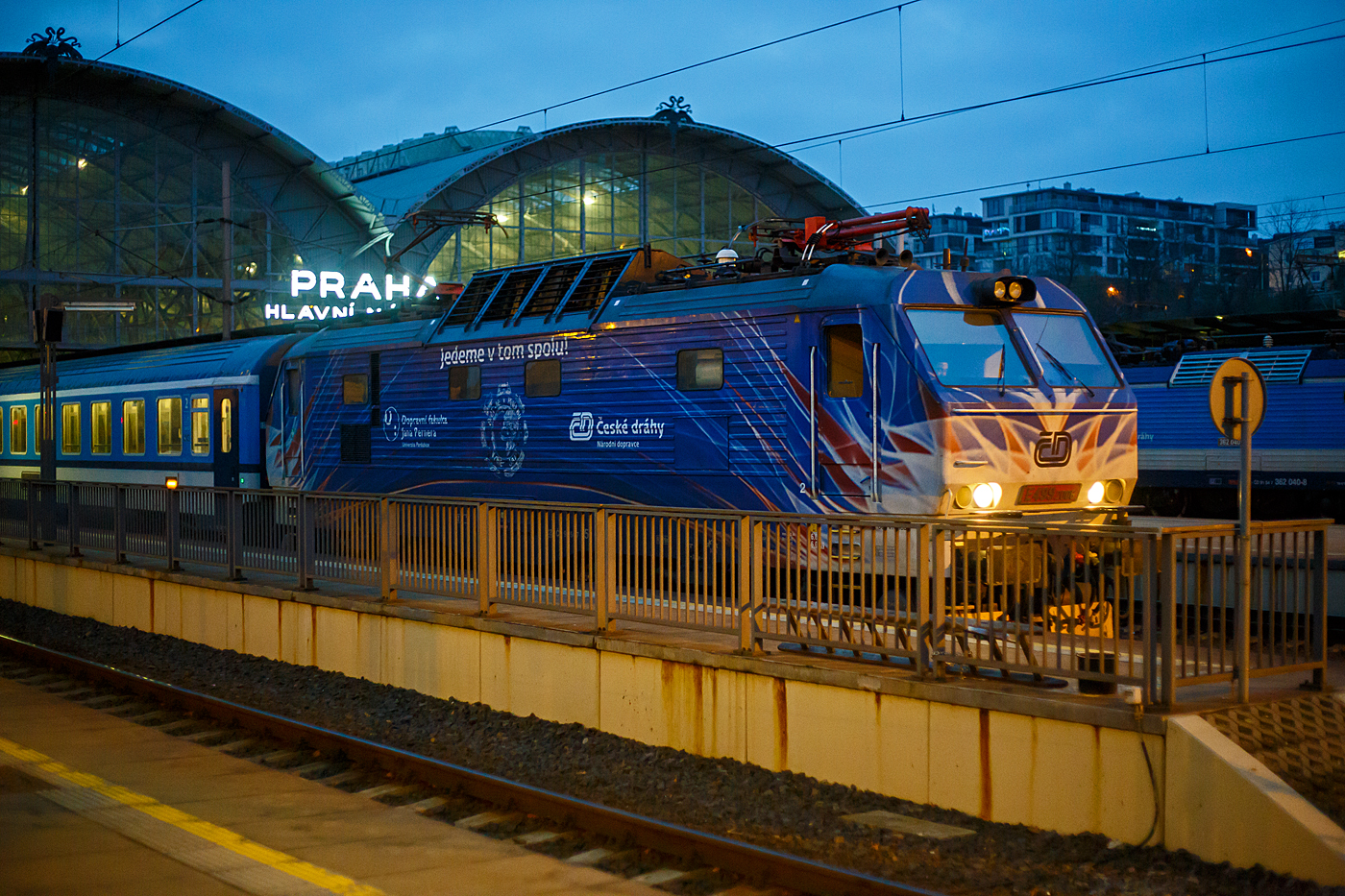 Die ČD E499 2006 alias ČD 151 006 (CZ- ČD 91 54 7 151 006-4), ex ČD 150 006, ex ČSD E 499.2006, steht am frühen Morgen des 24.11.2022, mit einem IC/ EC, im Prager Hauptbahnhof (Praha hlavní nádraží) zur Abfahrt bereit. Die 3 kV-Gleichstromlokomotive trägt eine schöne Werbelackierung Jedeme v tom spolu! (deutsch etwa: Machen wir es gemeinsam!).