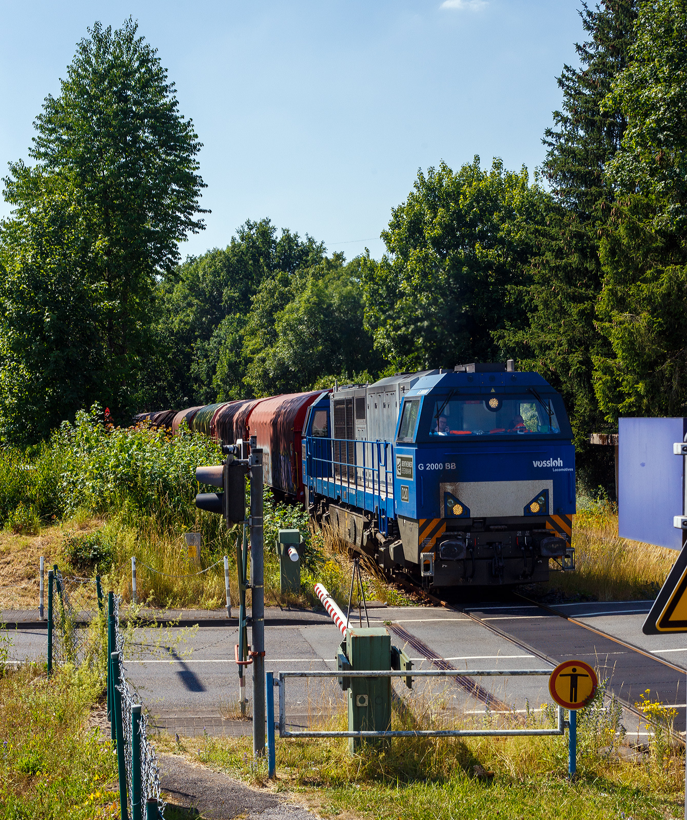 Die 272 408-6 / D20 der Bentheimer Eisenbahn AG (92 80 1272 408-6 D-BE), ex Rurtalbahn V 203 (92 80 1272 408-6 D-RTBC), eine Vossloh G 2000BB (mit symmetrischem Führerhaus) im Dienst für die KSW (Kreisbahn Siegen-Wittgenstein), fährt am 03 Juli 2025 mit einem Coilzug, über die Hellertalbahn, durch Alzdorf/Grünebacher Hütte in Richtung Herdorf. 