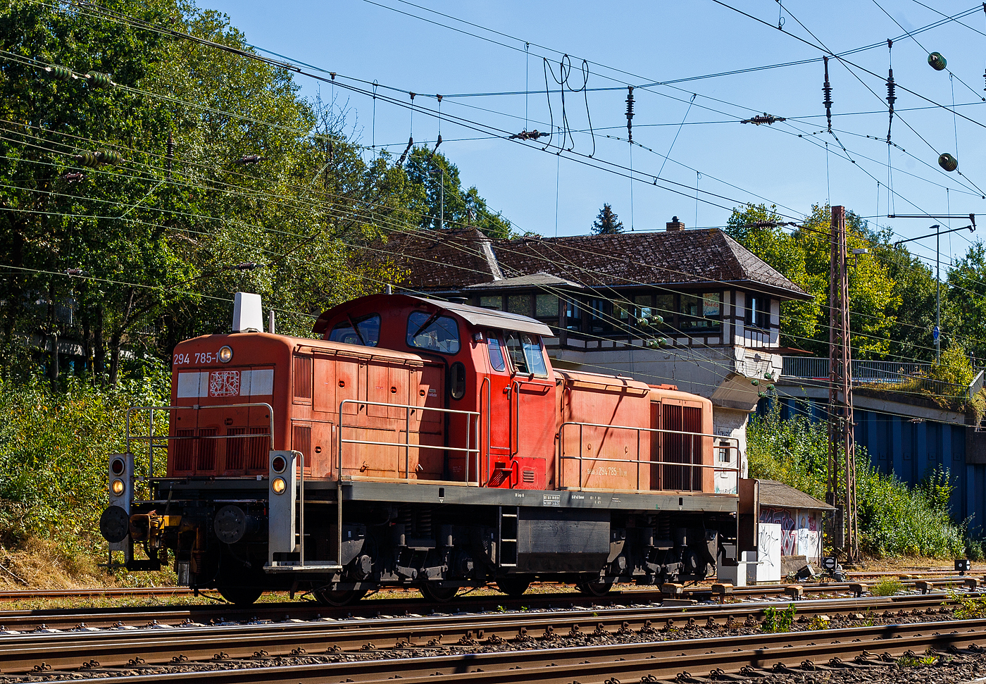 Die 294 785-1 (98 80 3294 785-1 D-DB) eine remotorisierte V 90 der DB Cargo AG rangiert am 07 September 2024 in Kreuztal zu ihrem Abstellplatz.

Die V 90 wurde 1972 von der Maschinenbau Kiel (MaK) unter der Fabriknummer 1000585 gebaut und als 290 285-6 an die DB - Deutsche Bundesbahn geliefert. 1996 erfolgte der Umbau mit Funkfernsteuerung und die Umzeichnung in DB 294 285-2. Die Remotorisierung mit einem MTU-Motor 8V 4000 R41, Einbau  einer neuen Lüfteranlage, neuer Luftpresser und Ausrüstung mit dem Umlaufgeländer erfolgten 2002 bei der DB Fahrzeuginstandhaltung Werk Chemnitz. Daraufhin erfolgte die Umzeichnung in 294 785-1.

Die Baureihe 290 (V60) wurde für den schweren Rangierdienst, sowie für Bedien- und Übergabefahrten konzipiert. Die Lok ist eine Weiterentwicklung aus den Streckenlokomotiven der Baureihenfamilie V100 (BR 211 und BR 212) der Deutschen Bundesbahn. Die V90 ist gegenüber der V100 deutlich schwerer und robuster im Rangierdienst. Ursprünglich war geplant, für den schweren Rangierdienst eine ballastierte Variante der V 100 mit verstärktem Rahmen zu beschaffen, die Fahrzeugauslegung war dafür aber nicht geeignet (die Achslast ließ sich so nicht auf die geforderten 20 t erhöhen). 

Die Maschinenbau Kiel (MaK) konstruierte daher die schwerere und längere V 90 und lieferte 1964/1965 zunächst 20 Vorserienlokomotiven mit dem 800 kW-Motor der Baureihe 211 und 70 km/h Höchstgeschwindigkeit. 1966 begann mit 290 021 die Serienlieferung, aus der bis Ende 1974 388 Exemplare hervorgingen. Die Serienloks besitzen den Motor MTU 12V 652 TA der Baureihe 212 (jedoch gedrosselt auf 800 kW) und sind 80 km/h schnell. Gegenüber der Vorserie wurde der Rahmen auf 14,32 Meter verlängert. Insgesamt wurden 408 Loks ausgeliefert. Neben MaK waren am Bau der Serienloks auch die Firmen Jung-Jungenthal, Henschel, Krupp und Deutz (KHD) beteiligt.

Die remotorisiert Maschinen haben nun einen MTU DM 8V 4000 R41 Motor mit 1.000 kW/1.360 PS Leistung bei 1.800 U/min, sie erfüllen die Abgasnorm UIC Kodex 624V, Stufe II.

Die Maschinen wurden in purpurrot (RAL 3004) abgeliefert und ab Mitte der 1970er Jahre in das neue Farbschema ozeanblau-elfenbein (RAL 5020, RAL 1014) umlackiert – im allgemeinen Sprachgebrauch auch ozeanblau-beige genannt. In der zweiten Hälfte der 1980er Jahre folgte das orientrote (RAL 3031) Farbschema, seit Ende der 1990er Jahre werden die Maschinen in das aktuelle verkehrsrot (RAL 3020) der Deutschen Bahn AG umlackiert. In der Praxis hielt sich in der Anfangszeit die purpurrote Lackierung länger als bei anderen Baureihen – erst ab dem Jahr 1988 war das ozeanblau-beige Farbschema dominant (bis 1996). Die verkehrsrote Umlackierung wurde dagegen zügig umgesetzt, sodass bereits im Jahr 2000 nahezu zwei Drittel der Lokomotiven diese Lackierung trugen.

Da die Motoren der Baureihen 290 und 212 baugleich sind, wurden besonders in den 1970er und 1980er Jahren Motoren zwischen den beiden Lokbaureihen ausgetauscht. Damit konnten Motoren mit hohen Laufleistungen aus dem Streckendienst einer sinnvollen Restnutzung in der 290 zugeführt werden, während umgekehrt bislang überwiegend im Rangierdienst schwächer belastete Motoren für die 212 zur Verfügung standen. Dieser Ringtausch führte dazu, dass etwa zur Jahrtausendwende umfangreiche Motorenbestände endgültig verschlissen waren. Deshalb wurde ein Remotorisierungsprogramm gestartet. Seit 2003 wurden Lokomotiven im Ausbesserungswerk Cottbus mit einem neuen 1.000 kW Motor des Typs 8V 4000 R41 von MTU ausgerüstet. Dabei wurde eine neue Zweikreis-Kühlanlage und ein neuer Luftpresser (Schraubenluftpresser mit hydrostatischem Antrieb) eingebaut. Der neue Motor spart trotz höherer Leistung im Mittel 5,4 Liter Diesel pro Betriebsstunde bei Volllast. Die Ordnungsnummer der remotorisierten Lokomotiven wurde um 500 erhöht. Um den Kraftstoffverbrauch weiter zu senken, hat DB Schenker Rail (heute DB Cargo) 2015 begonnen, die Lokomotiven mit einer Start-Stopp-Automatik auszurüsten.

Die Lokomotiven tragen heute die Hauptlast des Einzelwagenverkehrs der DB Cargo und sind in ganz Deutschland zu finden. Sie übernehmen die Abholung und Zustellung von Wagengruppen bei Gleisanschließern in der Fläche und den Verschub dieser Einheiten auf den Rangierbahnhöfen.

Umbau der Lokomotiven zur Baureihe 294 (mit KM- Funkfernsteuerung):
Ab 1995 wurden in großer Zahl Lokomotiven der Baureihe 290 mit einer anderen Art Funkfernsteuerung von Krauss-Maffei (KM) ausgerüstet. Bei ihr kann der nun „Lokrangierführer“ (Lrf) genannte Lokführer die Lok über ein um den Oberkörper gehängtes, vor dem Bauch getragenes Fernsteuerbediengerät (FBG) bedienen. Dies ermöglichte die Einsparung von Rangierpersonal und wurde zuvor schon bei den kleineren Rangierloks der Baureihen V 60 und Köf III angewandt. Die so umgebauten Loks der Baureihe 290 werden ab Umbau als Baureihe 294 bezeichnet. Der Umbau kostete seinerzeit rund 180.000 DM pro Lokomotive.

Die Lokomotiven haben auf dem Führerstand einen Funkrechner, der alle Signale vom Bedienteil empfängt. Dazu muss der Lrf den Funk manuell einschalten, dieses tut er mittels Schlüsselschalter am Rechnerschrank. Die Fahrzeuge mit KM-Fernsteuerung haben oberhalb der Führerstandsfenster auf jeder Seite eine Lampe (Sichtmelder), die leuchtet, sobald sie im Funkbetrieb fährt. Durch diese Fernsteuerung konnte viel Personal eingespart werden, weil der Lrf nun selber an der Spitze der Rangierabteilung anwesend sein kann. Folgende Funktionen können mit der Fernsteuerung ausgeführt werden: Fahren, Bremsen, Anfahren am Berg, Vkonstant (Fahrgeschwindigkeit automatisch beibehalten, nur bei V <12,5 km/h, durch Taster „Entriegeln“), Sanden, Pfeifen, Angleichen, Rangierkupplung öffnen (Motor- oder hinterer Vorbau) und Schnellbremsung. Des Weiteren ist das FBG mit einem Neigungssensor ausgestattet, der bei einer Neigung über 50 Grad nach etwa vier Sekunden eine Zwangsbremsung einleitet (angenommene Dienstunfähigkeit des Lrf). Diese Funktion kann durch einen Taster bei Stillstand überbrückt werden, wie z. B. beim Kuppelvorgang und dient der passiven Sicherheit des Lrf (jedoch lässt sich währenddessen keine Leistung aufschalten). Bei allen FBG-Varianten ist ein Schlagtaster eingebaut, der bei Betätigung eine Schnellbremsung auslöst (aktive Sicherheit).

Die beiden Lokomotiven 294 789 und 294 832 wurden 2019 im Instandhaltungswerk Cottbus zu Hybrid-Musterlokomotiven umgebaut. Dabei wurden die hydrodynamischen Getriebe ausgebaut und durch Elektromotoren und mechanische Getriebe ersetzt, die durch Akkus bzw. den Fahrdiesel gespeist werden. Das Umbauprojekt mit dem Namen HELMS (Hybrid ELectro-Mechanical Shunter) erfolgt in Zusammenarbeit mit der japanischen Firma Toshiba. Sie tragen die neue Baureihenbezeichnung 1094. Siehe: http://hellertal.startbilder.de/name/galerie/kategorie/deutschland~hybridloks~1094-helms-ex-v-90.html 

TECHNISCHE DATEN:
Hersteller: MaK, Jung-Jungenthal, Henschel, Krupp, Deutz (KHD), Rheinstahl
Spurweite: 1.435 mm (Normalspur)
Achsanordnung: B'B'
Länge über Puffer: 14.320 mm
Breite: 3.100 mm
Drehzapfenabstand: 7.000 mm
Achsabstand im Drehgestell: 2.500 mm
Treibraddurchmesser: 	1.100 mm (neu)
Höchstgeschwindigkeit: 80 km/h Streckengang / 40 km/h Rangiergang 
kleinste Dauergeschwindigkeit: 9 km/h Streckengang / 3 km/h Rangiergang
Anfahrzugkraft: Schnellgang: 188 kN / Langsamgang: 236 kN
Dauerzugkraft: 184 kN
Getriebe: Voith L206rs

Motorhauptdaten der Uraufführung (BR 290):
Motorbauart: wassergekühlter MTU V12-Zylinder-Dieselmotor mit Vorkammereinspritzung, Abgasturbolader und Kolbenkühlung.
Motortyp: MTU MB 12 V 652 TA 10 (wie Daimler-Benz MB 835 Ab)
Nennleistung:  800 kW / 1.100 PS (gedrosselt)
Drehzahl max.:  1.400  U/min   
Bohrung/Hub: 190/230 mm
Hubraum: 78,25 Liter.
Turboladertyp: BBC VTR 250-Abgasturbolader
Gewicht Dieselmotor incl. Regler (trocken): ca. 4.500 kg.

Motormerkmale: Kurbelgehäuse aus Grauguss. Geschmiedete Kurbelwelle siebenfach gleitgelagert, Pleuelstangen gleitgelagert. Zweiteilige Kolben (Version „TA“). Zylinderköpfe mit je zwei Ein- und Auslassventilen und zentraler Vorkammer. Ventilsteuerung über eine untenliegende Nockenwelle, Rollenstößel, Stoßstangen und Kipphebel, Schließen der Ventile durch Ventilfedern. 

Motorhauptdaten der remotorisierte V 90, BR 294.5 (Quelle: MTU):
Motorbauart: MTU 8-Zylinder-Diesel-V-Motor 90° mit Common-
Rail-Einspritzsystem, Abgas-Turbolader und Ladeluftkühlung
Motortyp:   8V 4000 R41 
Nennleistung:  1.000 kW / 1.341 PS (gedrosselt)
Drehzahl max.:  1.800  U/min   
Bohrung/Hub: 165/190 mm
Hubraum: 32,5l
Kraftstoffverbrauch bei Nennleistung: 249,4 l/h
Abgas-Emission :  UIC Kodex 624V, Stufe II
Länge: 1.915 mm
Breite: 1.380 mm
Höhe: 1.800 mm
Gewicht (trocken): 4.700 kg

Getriebe und Leistungsübertragung:
Das hydraulische Getriebe L206rs von Voith hat zwei Wandlergänge. Ein mechanisches Nachschaltgetriebe ermöglicht die Wahl zwischen einem Schnell- und einem Langsamgang sowie den Wechsel der Fahrtrichtung. Um feinfühlige Langsamfahrten zu ermöglichen, hat das Getriebe eine stufenlos regelbare Wandlerteilfüllung. Die Traktionsleistung am Getriebeausgang beträgt 639 kW (869 PS). Die Leistungsübertragung auf die Achsgetriebe erfolgt dann über Gelenkwellen.
Bremse: KE-GP-mZ
Tankinhalt: 3.200 Liter

Konstruktionsmerkmale:
Die folgenden Erläuterungen zur Ausstattung der V 90 beziehen sich soweit nicht anders angegeben auf den Auslieferungszustand. Nach Umbau zur Funklok und Remotorisierung weicht die technische Ausrüstung heute erheblich davon ab.

Der Rahmen besteht aus Walzprofilen und Stahlgussteilen, wegen der angestrebten 20 t Achslast war kein Leichtbau nötig. Zusätzlich wurden sechs Tonnen Ballast eingebaut.

Die Vorbauten sind schmaler als bei der V 100, um eine bessere Sicht beim Rangieren zu ermöglichen. Der längere vordere Vorbau enthält Kühlanlage, Vorwärmgerät und den Dieselmotor. Im hinteren Vorbau befinden sich Anlasslichtmaschine, Druckluftanlage, Batterien und der Betriebsbehälter der Kraftstoffanlage. Unter dem Führerhaus befinden sich die Kraftstoff-Hauptbehälter und das hydraulische Getriebe. Das Führerhaus entspricht weitgehend dem der Baureihe V 60.

In den Drehgestellen werden die Achslager durch Metall-Gummi-Federn (Megi-Federn) geführt. Der Lokrahmen greift über Drehtürme mit Durchlässen für die Gelenkwellen zu den Achsgetrieben in die Drehgestelle ein. Der Rahmen stützt sich über Doppel-Schraubenfedern auf die Drehgestelle ab. Die Auslenkung der Drehgestelle im Bogen erfolgt ohne Gleitstücke.

Der Dieselmotor MTU 652 TA 10 ist ein wassergekühlter 12-Zylinder-Motor in V-Form mit Vorkammereinspritzung, Abgasturbolader und Kolbenkühlung.

Die Kraftstoffpumpe fördert den Kraftstoff aus den Hauptbehältern unter der Lok zunächst in einen hochliegenden Betriebsbehälter und von dort weiter zu den Einspritzpumpen. Ein Überströmventil begrenzt den Überdruck im Vorlauf der Einspritzpumpen auf 0,6 bar. Bei Ausfall der Kraftstoffpumpe kann der Betriebsbehälter per Handpumpe nachgefüllt werden und mit Fallkraftstoff weitergefahren werden. Die Loks verbrauchen im Leerlauf etwa 12 Liter Dieselkraftstoff pro Stunde, unter Volllast etwa 230 Liter pro Stunde.

Zur Rückkühlung des Motorkühlwassers sind hydrostatische Lüfteranlagen von Behr oder Voith vorhanden. Da die Lokomotive anders als die V 100 über keinen Dampfheizkessel verfügt, den man zur Kühlwasservorwärmung nutzen könnte, ist stattdessen ein kleiner, dieselgefeuerter Warmwasserkessel von Hagenuk, oder später ein Vorwärmgerät der Firma Webasto oder A.S.T. eingebaut.

Das hydraulische Getriebe Voith L206rs hat zwei Wandlergänge. Ein mechanisches Nachschaltgetriebe ermöglicht die Wahl zwischen einem Schnell- und einem Langsamgang sowie den Wechsel der Fahrtrichtung. Um feinfühlige Langsamfahrten zu ermöglichen, hat das Getriebe eine stufenlos regelbare Wandlerteilfüllung.

Der Führertisch ist beidseitig bedienbar. Die Steuerung von Motor und Getriebe erfolgt pneumatisch. Durch Drehen des Fahrschalters wird stufenlos über ein Feinregelventil ein bestimmter Steuerdruck in das System gegeben. Dieser beeinflusst die Schaltvorgänge im hydraulischen Getriebe und wirkt am Motor auf den Drehzahlregler R 32 p von Maybach mit drehzahlabhängiger Füllungsbegrenzung ein.

Quellen: www.loks-aus-kiel.de; Wikipedia; www.eib-t.de und MTU
