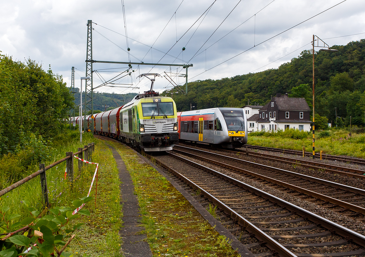 Die an die Dortmunder Eisenbahn GmbH (DE) vermietete SIEMENS Vectron Dual Mode 248 034-1  Phoenix  (90 80 2248 034-1 D-DE) der Captrain Deutschland GmbH fährt am 01 Juli 2024, mit einem Coilzug (Wagen der Gattung Shimmnis-ttu der Ermewa) durch Scheuerfeld/Sieg in Richtung Köln. Rechts wir der an die WEBA (Westerwaldbahn des Kreises Altenkirchen GmbH) vermietete Stadler GTW 2/6 VT 509 109 der HLB (Hessische Landesbahn GmbH), auf Rangierfahrt, überholt. 

Hinten rechts der ehem. Kleinbahnhof Scheuerfeld/Sieg der WEBA (Westerwaldbahn des Kreises Altenkirchen GmbH).