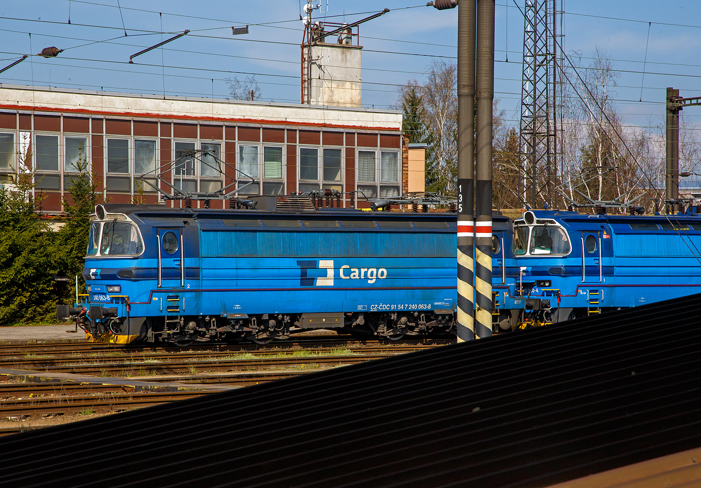 Die beiden elektrischen Lokomotiven für Wechselstrom (25 kV/50 Hz) 240 063-8 (CZ-ČDC 91 54 7 240 063-8) und die 240 060-4 (CZ-ČDC 91 54 7 240 060-4) der ČD Cargo, a.s. stehen am 21.04.2023 beim Bahnhof Sokolov (bis 1948 Falknov nad Ohří, deutsch Falkenau an der Eger). Da unsere Zug im Bahnhof hielt, heiß es schnell aus dem Sitz, Tür auf und ein Bild machen, daher war leider der Mast und das Doch vom Treppenaufgang im Weg.

Die BR 240, ex ČSD-Baureihen S 499.0 bzw. S 499.1 sind elektrische reine AC-Lokomotiven für den Personen- und Güterzugverkehr der einstigen Tschechoslowakischen Staatsbahn ČSD für das mit 25 kV 50 Hz Wechselstrom elektrifizierte Streckennetz im Süden und Westen der damaligen Tschechoslowakei. Die S 499.1 wurden aus der S 489.0 entwickelt, von der sie sich vor allem durch die höhere Höchstgeschwindigkeit von 140 km/h unterscheidet, so ist diese eher für Schnell- und Personenzüge. Die S 499.0 (BR 240) hat eine Höchstgeschwindigkeit von 120 km/h und ist so eher vor Güterzügen.

Von den Lokomotiven der Reihe S 499.0 (Škoda 47E) wurden 1968/69 120 Loks von Škoda in Pilsen hergestellt. Diese Lokomotiven wurden auf tschechischer Seite in Pilsen, Cheb und České Budějovice (Budweis), auf slowakischer Seite in Bratislava und Nové Zámky stationiert. 

Für die Bespannung der Expresszüge zwischen Kutná Hora und Bratislava sowie zwischen Zvolen–Nové Zámky wurden 1970 dann 25 Lokomotiven der Reihe S 499.1, mit einer höheren Höchstgeschwindigkeit von 140 km/h beschafft. Nach deren Beschaffung endete die Fertigung von Lokomotiven mit Lokkästen aus glasfaserverstärktem Kunststoff. Die wichtigsten Änderungen gegenüber der S 489.0 sind das Übersetzungsverhältnis zwischen Fahrmotorritzel und Großrad von 1:3,2, die elektrische Bremse, durch deren Dachaufbau sie von den Lokomotiven der Reihe S 489.0 zu unterscheiden sind, und eine pneumatische Bremse DAKO L/R. Ansonsten sind beide Baureihen identisch. Mit dem Erscheinen der Mehrsystemlokomotive ES 499.0 und deren Nachfolger übernahmen diese Maschinen dann die Schellzüge und Lokomotiven der Reihe S 499.1 wurden daraufhin in die Reihe S 499.0 zurückgebaut. Im Jahr 1988 wurden alle Lokomotiven einschließlich der ehemaligen Reihe S 499.1 in die Baureihe 240 umgezeichnet.

Nach der Auflösung der Tschechoslowakei zum 01.01.1993 verblieben die meisten Lokomotiven bei der Eisenbahn der Slowakischen Republik (ŽSR), heute ZSSK (Žeľezničná spoločnosť Slovensko, a.s.). Nur ein kleiner Teil kam zu den Tschechischen Bahnen (ČD), die sie zum Teil zu Zweisystemlokomotiven der ČD BR 340 zwischen 2001 und 2003 umbaute.

TECHNISCHE DATEN:
Herstellertyp: Škoda 47E
Baujahre: 1968–1970
Anzahl: 145
Spurweite: 1.435 mm (Normalspur)
Achsformel:  Bo'Bo'
Länge über Puffer: 16.440 mm
Drehzapfenabstand: 7.800 mm
Achsabstand im Drehgestell: 2.800 mm
Treibraddurchmesser: 1.250 mm (neu)
Dienstgewicht:  85,0 t
Radsatzfahrmasse:  21,25 t
Höchstgeschwindigkeit:  120 km/h (140 km/h S 499.1)
Stundenleistung:  3.200 kW
Dauerleistung:  3.080 kW
Anfahrzugkraft: 255 kN
Stromsystem:  25 kV 50 Hz Wechselstrom (AC)
Fahrmotoren:  4 Stück vom Typ Škoda 9 AL 4446 iP
Antrieb:  Škoda Hohlwellenantrieb