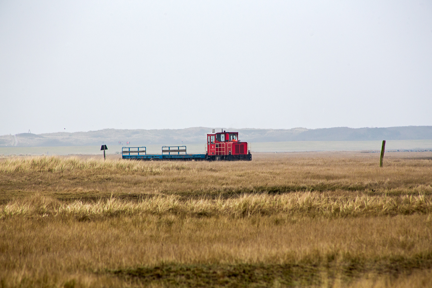 Die DB 399 108-0 (98 80 3399 108-0 D-DB) der Wangerooger Inselbahn (der DB Fernverkehr AG bzw. der SIW - Schifffahrt und Inselbahn Wangerooge) drückt am 12 März 2024 einen kurzen leeren Güterzug (zwei Flachwagen) vom Westanleger Wangerooge in Richtung zum Bahnhof Wangerooge. 

Die meterspurige Lok wurde 1999 von SCHÖMA - Christoph Schöttler Maschinenfabrik GmbH in Diepholz unter der Fabriknummer 5600 für die Inselbahn Wangerooge der Deutsche Bahn AG gebaut und geliefert.
