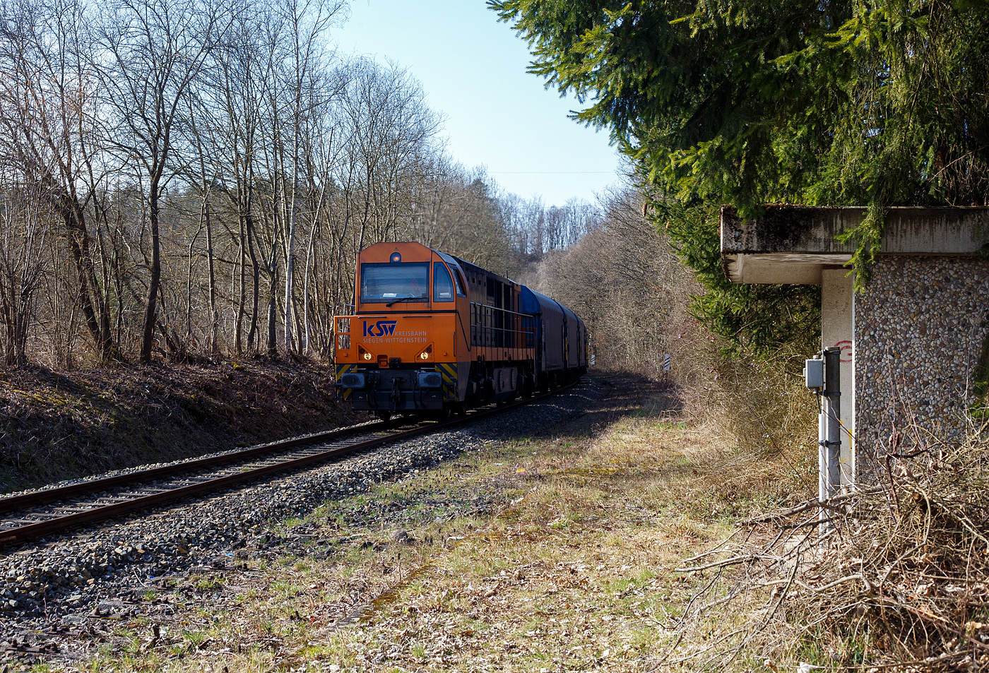 Die KSW 43 (92 80 1273 018-2 D-KSW), die asymmetrische Vossloh G 2000 BB der KSW (Kreisbahn Siegen-Wittgenstein) fährt am 10 März 2025, mit einem beladen Coilzug (VTG Coilwagen der Gattung Shimmns-ttu, VTG Bez. F46.520D) vom Hafen Duisburg kommend über die KBS 462 „Hellertalbahn“ durch Alsdorf in Richtung Herdorf, hier beim Haltepunkt (Hp). 

Bis 1987 war der Abschnitt Betzdorf–Herdorf noch zweigleisig, so war hier an meinem Standort, bis dahin der Bahnsteig für die Fahrtrichtung der Züge nach Betzdorf.