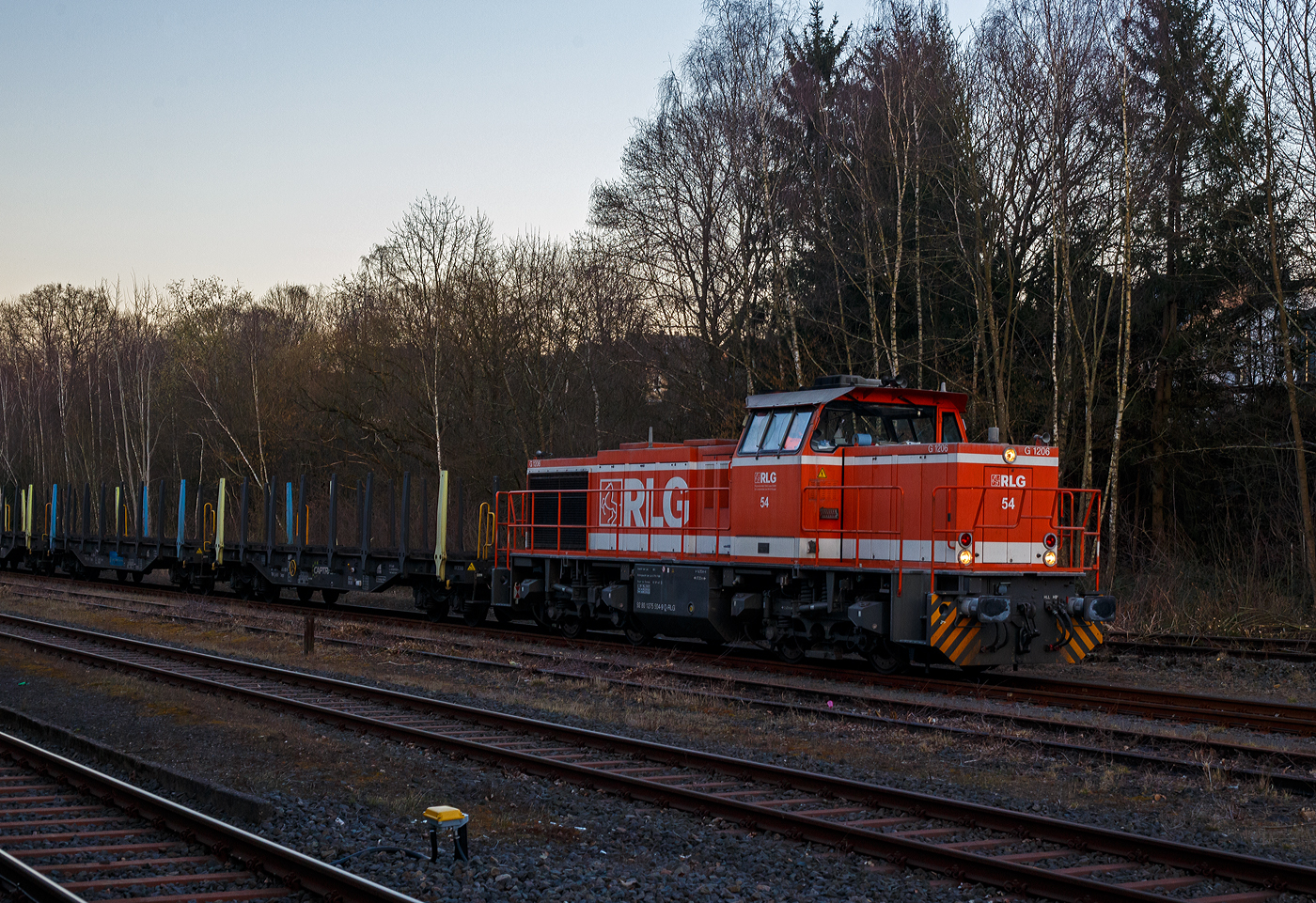 Die RLG 54 / 275 504-9 (92 80 1275 504-9 D-RLG) eine MaK G 1206 der RLG - Regionalverkehr Ruhr-Lippe GmbH (Soest), vermietet ans Schwesterunternehmen WLE - Westfälische Landes-Eisenbahn GmbH, kommt am 18. März 2025 auf ihrer Heimreise mit einem leeren Güterzug (Schwerlastwagen) von der Salzgitter Mannesmann Precision GmbH in Burbach-Holzhausen über die Hellertalbahn durch Herdorf. Hier im Bahnhof Herdorf hat sie, wegen der eingleisigen Strecke, erstmal Hp 0, bevor es in Richtung Betzdorf weitergeht.

Die G 1206 wurde 2008 von Vossloh in Kiel unter der Fabriknummer 5001638 gebaut. Sie war die erste wieder mit einen MTU gebaute G 1206. So hat sie einen wassergekühlten V12-Zylinder-Dieselmotor mit Abgasturbolader und Ladeluftkühlung vom Typ MTU mit einer Leistung von 1.500 kW (bei 1.800 U/min).

TECHNISCHE DATEN der G 1206:
Spurweite: 1.435 mm
Antriebart:  dieselhydraulisch
Achsfolge: B'B' 
Länge über Puffer: 14.700 mm
Drehzapfenabstand: 7.200 mm
Achsabstand im Drehgestell: 2.400 mm
größte Breite: 3.080 mm
Höhe über Schienenoberkante: 4.220 mm
Raddurchmesser neu: 1.000 mm
Motor: MTU 12 Zylinder 4-Takt Dieselmotor mit Abgasturbolader und Ladeluftkühlung vom Typ 12V 4000 R41
Leistung: 1.500 kW bei1.800 U/min
Strömungsgetriebe: Voith L 5r4 zseU2
Anfahrzugkraft: 267 kN
Höchstgeschwindigkeit: 100 km/h
kleinster befahrbarer Gleisbogen:	60 m
Dienstgewicht: 88 t
Kraftstoffvorrat: 3.150 l