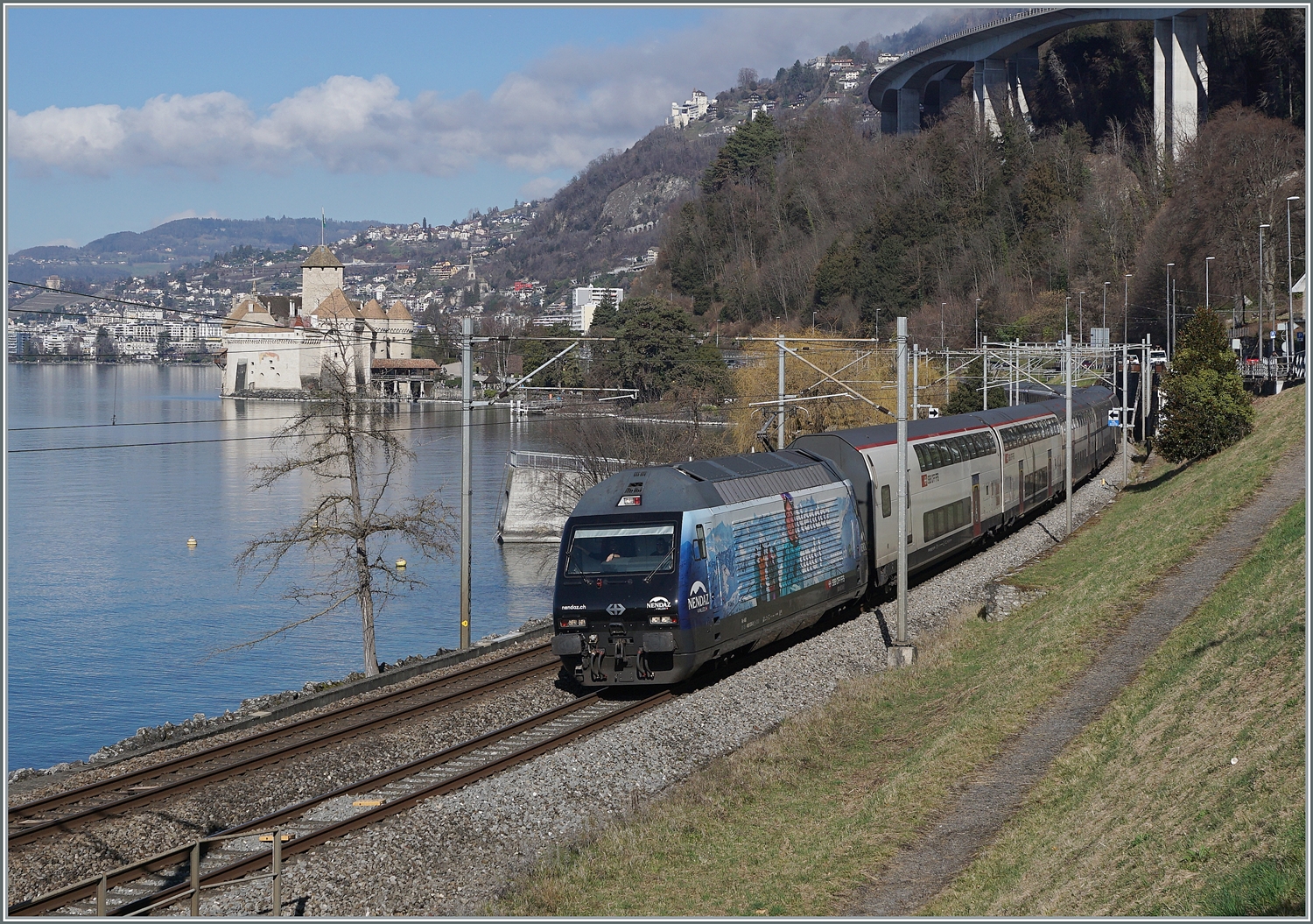 Die SBB Re 460 078 mit der Werbung f�r Nendaz ist bei Villeneuve mit einem IR90 auf dem Weg in Richtung Brig. 

13. Feb. 2024 