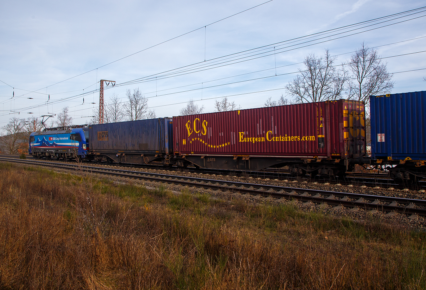 Hinter der an die SBB Cargo International AG vermietete SIEMENS Vectron MS 193 530  Po , der sechsachsige Drehgestell-Gelenk-Containertragwagen-Einheit (6-achsiger Containertragwagen), 3 54 4962 273-7 CZ-GTSL der Gattung Sggmrss, der italienischen GTS Logistic (Bari), am 22.02.2023 im Zugverband bei der Zugdurchfahrt in Wilnsdorf-Rudersdorf (Kr. Siegen), hier beladen mit zwei Containern.

TECHNISCHE DATEN:
Spurweite: 1.435 mm
Anzahl der Achsen: 6 in drei Drehgestellen
Länge über Puffer: 29.590 mm
Drehzapfenabstand: 2 x 11.995 mm
Achsabstand im Drehgestell: 1.800mm
Laufraddurchmesser: 920 mm (neu)
Ladelänge : 2 x 13.820mm (2 x 45 ft)
Höhe der Ladeebene über SOK: 1.155 mm
Eigengewicht: ca. 28.000 kg
Max. Zuladung bei Lastgrenze S: 107,0 t (ab Streckenklasse D)
Max. Zuladung bei Lastgrenze SS: 92,0 t (ab Streckenklasse C)
Max. Geschwindigkeit: 100 km/h (Lastgrenze SS oder leer 120 km/h)
Kleinster bef. Gleisbogenradius: R 75 m
Verwendungsfähigkeit: TEN-GE