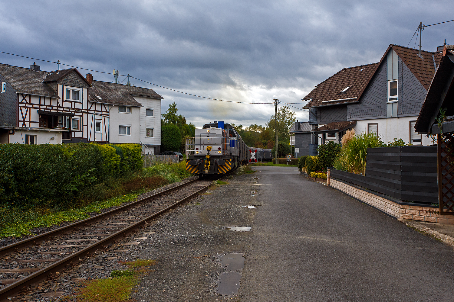 Nun hat die KSW 47 (92 80 1271 027-5 D-KSW), ex D 2 der HFM, eine Vossloh G 1000 BB der KSW (Kreisbahn Siegen-Wittgenstein), den Coilzug übernommen und zieht diesen nun vom KSW Rbf Herdorf weiter zu den Schäfer Werke KG am Pfannenberg in Neunkirchen-Salchendorf. Hier geht es gerade in Neunkirchen-Struthütten am 18 September 2025 zwischen den Häuser und Hecken hindurch. 

Auch wenn hierdurch, mehrmals täglich, die Anwohner genervt werden, zu Einem durch die Rollgeräusche und vor allem durch das erforderliche Pfeifen (Hupen) der Loks, wegen der vielen Bahnübergänge. Aber dennoch ist es schon lange praktifizierter Umweltschutz, denn mit allein dieser Zug ersetzt 40 bis 50 LKW. Übrigens diese Bahnstrecke der ehemaligen Freien Grunder Eisenbahn AG (auch bekannt als „Talbahn“) gibt es seit 1904, heute gehört sie als Betriebsstätte FGE -Freien Grunder Eisenbahn zur KSW Kreisbahn Siegen-Wittgenstein GmbH und wird als Freien Grunder Eisenbahn NE 447 (DB - Streckennummer 9275) geführt.

Mit einer eigenen Schieneninfrastruktur im Kreis Siegen-Wittgenstein, die mehr als 30 Kilometer umfasst, verfügt die KSW über wichtige Kapazitäten im wachsenden Güterverkehr. Auch wenn in Deutschland der Schienen-Güterverkehr geringer geworden ist, so ist er hier auf der „Talbahn“ die letzten Jahre ungemein gewachsen. 

Früher gab es ich Siegen (Eintracht) noch einen Abschnitt, wo die KSW bzw. frühere Siegener Kreisbahn auf der Eiserfelder Straße mit Läute (Glocke) fuhr, so wurde diese Bahn auch gerne im Volksmund „Bimmelbahn“ genannt.