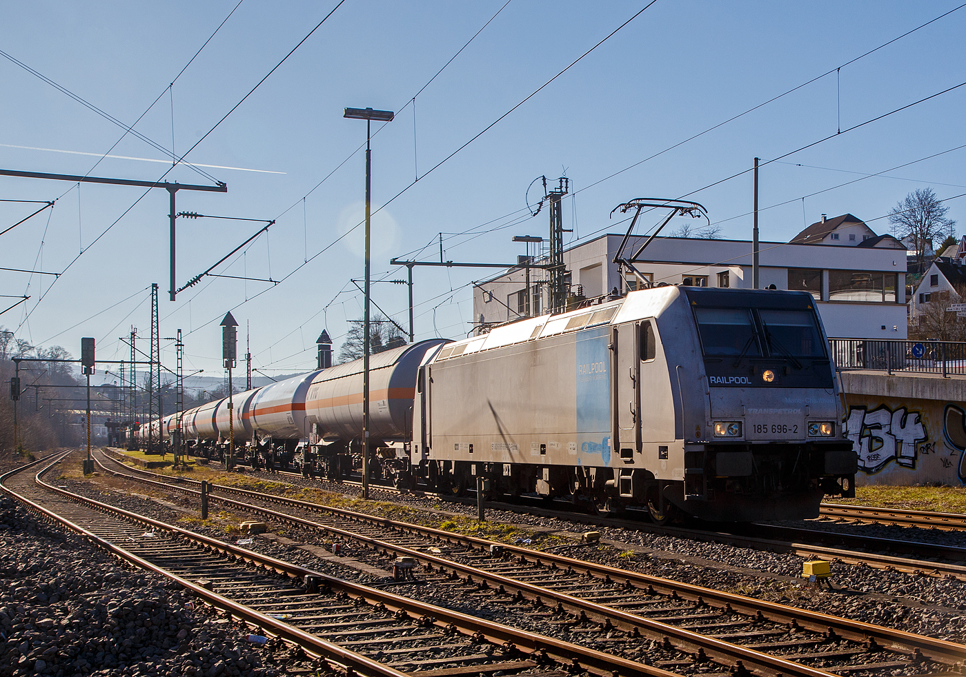 Nun sind die Schranken am Bü 343 geschlossen und sie hat Hp 1 oder 2...
Die 185 696-2 „Marie-Chanthou“ (91 80 6185 696-2 D-Rpool) der Railpool fährt am 14.02.2023 mit einem Druckgas-Kesselwagenzug über die Siegstrecke (KBS 460), durch Niederschelderhütte in Richtung Siegen.

Die TRAXX F140 AC2 wurde 2010 von Bombardier in Kassel unter der Fabriknummer 34722 gebaut und an die Railpool geliefert. Die Lok ist für Deutschland und Österreich zugelassen. Die ehemaligen Zulassungen für Schweden und Norwegen sind nun durchgestrichen.