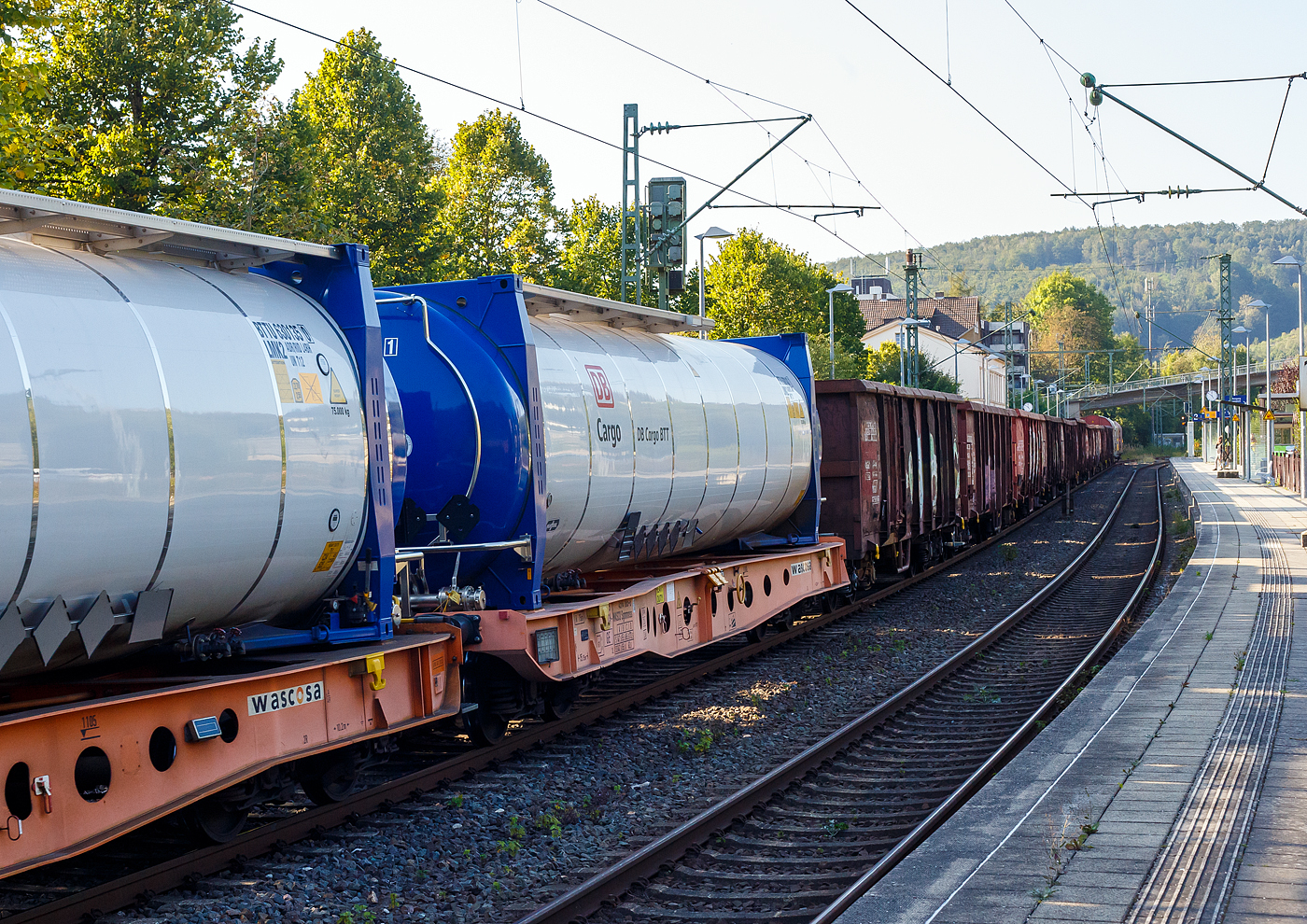 Vierachsiger 45‘ Drehgestell-Containertragwagen, 33 85 4594 065-6 CH-WASCO, der Gattung Sgmmnss, beladen mit 45 Fuß VanHool- Spezial-Tankcontainer der DB Cargo BTT, am 17 September 2024 im Zugverband bei der Durchfahrt im Bahnhof Kirchen (Sieg).

Die Wascosa 45‘ Containertragwagen Sgmmnss sind für den Transport von intermodalen Ladeeinheiten. Die Wagen wurden von Tatravagónka a.s. in Poprad (Slowakei) gebaut. Diese Wagen sind Bestandteil des Wascosa flex freight systems®. So sind neben den Tankcontainern auch u.a. Niederbord- oder Hochbord-Aufbauten, Rungenaufbauten für den Holztransport möglich. 

WASCOSA hat sich zum Ziel gesetzt der fortschrittlichste Güterwagenvermieter zu sein. Das WASCOSA flex freight system® wurde speziell für diejenigen Teilnehmer am Schienengüterverkehr entwickelt, welche die langfristige Produktivität und Wirtschaftlichkeit ihres eingesetzten Rollmaterials erhöhen und die Anzahl der eingesetzten Güterwagen optimieren möchten. Ziel des Projektes war es, einen Güterwagen zu entwickeln, der für unterschiedliche Arten von Ladegütern ganzjährig eingesetzt werden kann und somit über den gesamten Life Cycle des Wagens hinweg eine kontinuierlich hohe Beschäftigung und ebenso hohe Produktivität ermöglicht.

BASF und DB Cargo setzen auf neue Tank-Container, diese werden vom belgischen Hersteller Van Hool hergestellt. Hier dieser 45‘-Tankcontainer DB Cargo BTT GmbH (der Gefahrgutspezialist der DB Cargo) haben beladen ein Gesamtgewicht von 75.000 kg, bei einem Eigengewicht von ca. 9 t eine Nutzlast von 66 t bzw. ein Fassungsvermögen von 63.000 Liter. Die Tanks sind im Tankcode L4BH ausgeführt, das heißt:

Zul. Betriebsüberdruck: 3,0 bar
L= Tank für Stoffe in flüssigem Zustand (flüssige Stoffe oder feste Stoffe, die in geschmolzenem Zustand zur Beförderung aufgegeben werden)
4= zutreffender Mindestprüfdruck in bar
B = Tank mit Bodenöffnungen mit 3 Verschlüssen für das Befüllen oder Entleeren 
H = luftdicht verschlossener Tank

Der 45‘ Containertragwagen Sgmmnss («5L» Tragwagen):
Vorteile:
• Laufleistungsstark durch den Einsatz moderner Scheibenbremsen
• Besonders leise, nur 78 dB(A)
• Besonders leicht mit einem Eigengewicht von 16,5 t
• Life-Cycle-Cost orientiert, durch schnell austauschbare Komponenten
• Logistikfähig durch den Einsatz von Telematik
• Wascosa flex freight system®  für denTransport verschiedener Güter durch die Kombination des besonders leichten Containertragwagens mit einem individuellen Oberbau
• Die Kombination des Wagens mit 45‘ Tankcontainern kann Kesselwagen ersetzen und ermöglicht eine unabhängige Instandhaltung beider Komponenten
• Transport von Tankcontainern im Einzelwagenverkehr mit bis zu 2,70 m Containerhöhe im G1-Profil

TECHNISCHE DATEN des Wagens:
Gattung: Sgmmnss 45´
Gattungskennzahl: 4594
Spurweite: 1.435 mm (Normalspur)
Achsenanzahl : 4 (in 2 Drehgestellen)
Länge über Puffer : 15.145 mm
Drehzapfenabstand: 10.185 mm
Achsabstand in den Drehgestellen: 1.800 mm
Raddurchmesser: 920 mm (neu) / 840 mm (abgenutzt)
Länge Ladefläche: 13.815
Höhe der Ladefläche über SOK: 1.105 mm
Eigengewicht : ca. 16.500  kg
Max. Zuladung bei Lastgrenze S: 73,5 t (ab Streckenklasse D)
Max. Zuladung bei Lastgrenze SS: 63,5  t (ab Streckenklasse C)
Höchstgeschwindigkeit: 100 km/h Lastgrenze S / 120 km/h bei Lastgrenze SS und leer)
Drehgestell: TVP NG-DBS (Y25Lsso-D)
Radsätze: Rl 706
Bremse: Knoor KE-GP-A (D)
Bremssohle: Jurid 707 (oder Becorit BM41NT)
Handbremse: Ja
Kleinster befahrbarer Gleisbogen: R = 75m (im Zugverband R = 150 m)
Intern. Verwendungsfähigkeit: TEN GE / G1