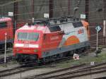 Mit Tele so gut es ging durch viele Fahrdrähte durch: 120 112-8 mit Märklin-Werbung vor dem Lokschuppen in Ulm am 19.05.2012.